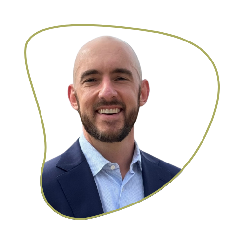 A smiling man with a beard and bald head, dressed in a blue blazer and light blue shirt, against a green background.