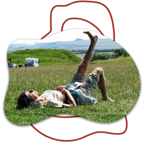 A person lying on the grass in a field with a hill and cloudy sky in the background.