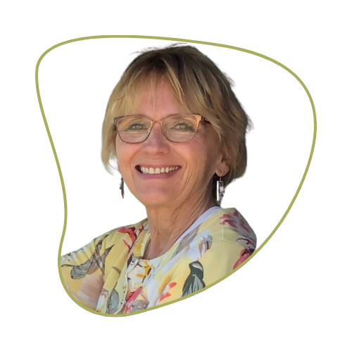 A smiling middle-aged woman with short blonde hair and glasses, wearing a colorful patterned blouse, against a green background.