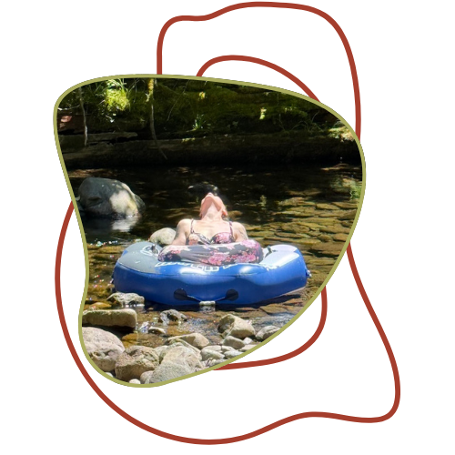 Child floating on an inflatable in a shallow river with rocks and trees in the background.