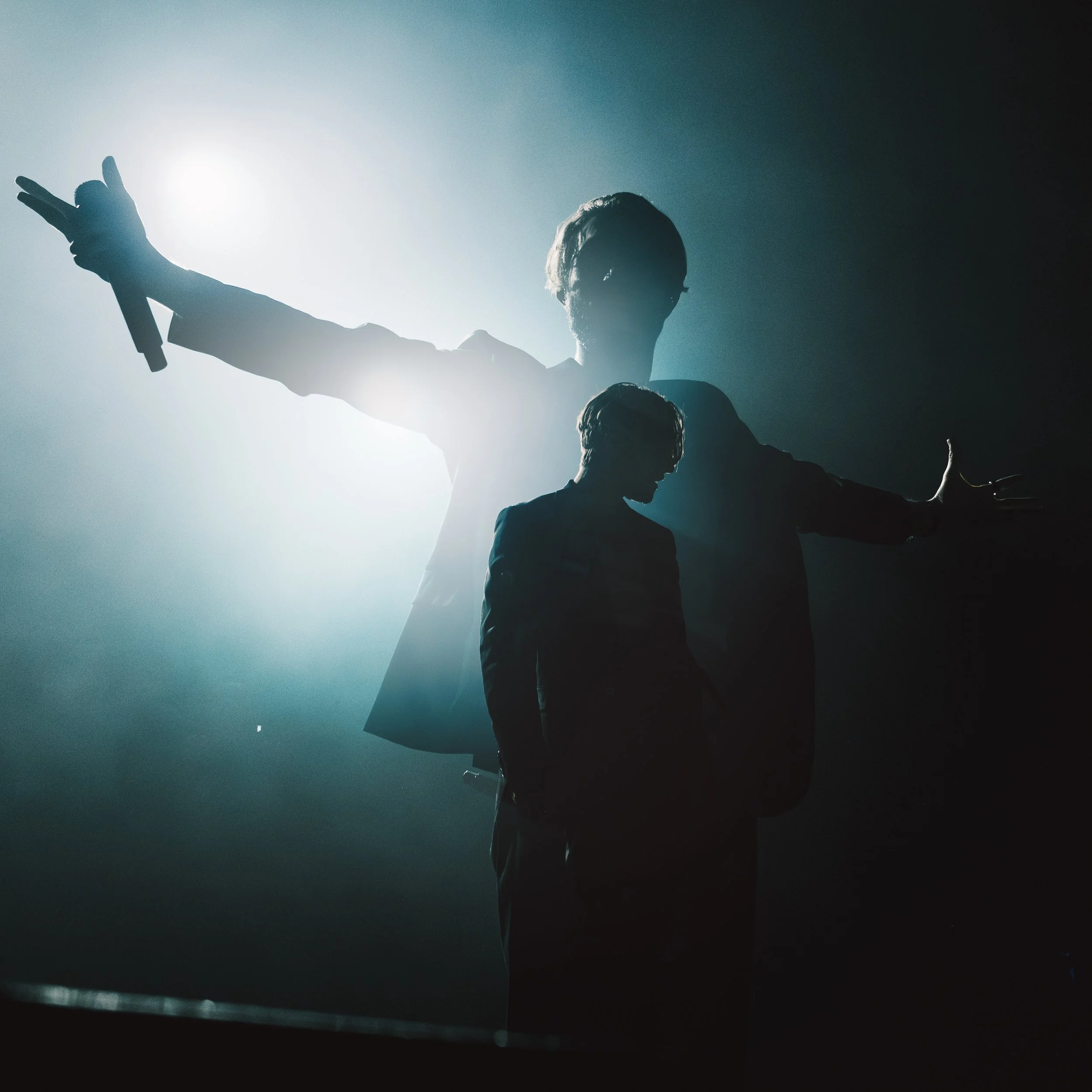 Silhouettes of two people, one adult and one child, on a stage with bright light behind them, creating shadowed outlines.