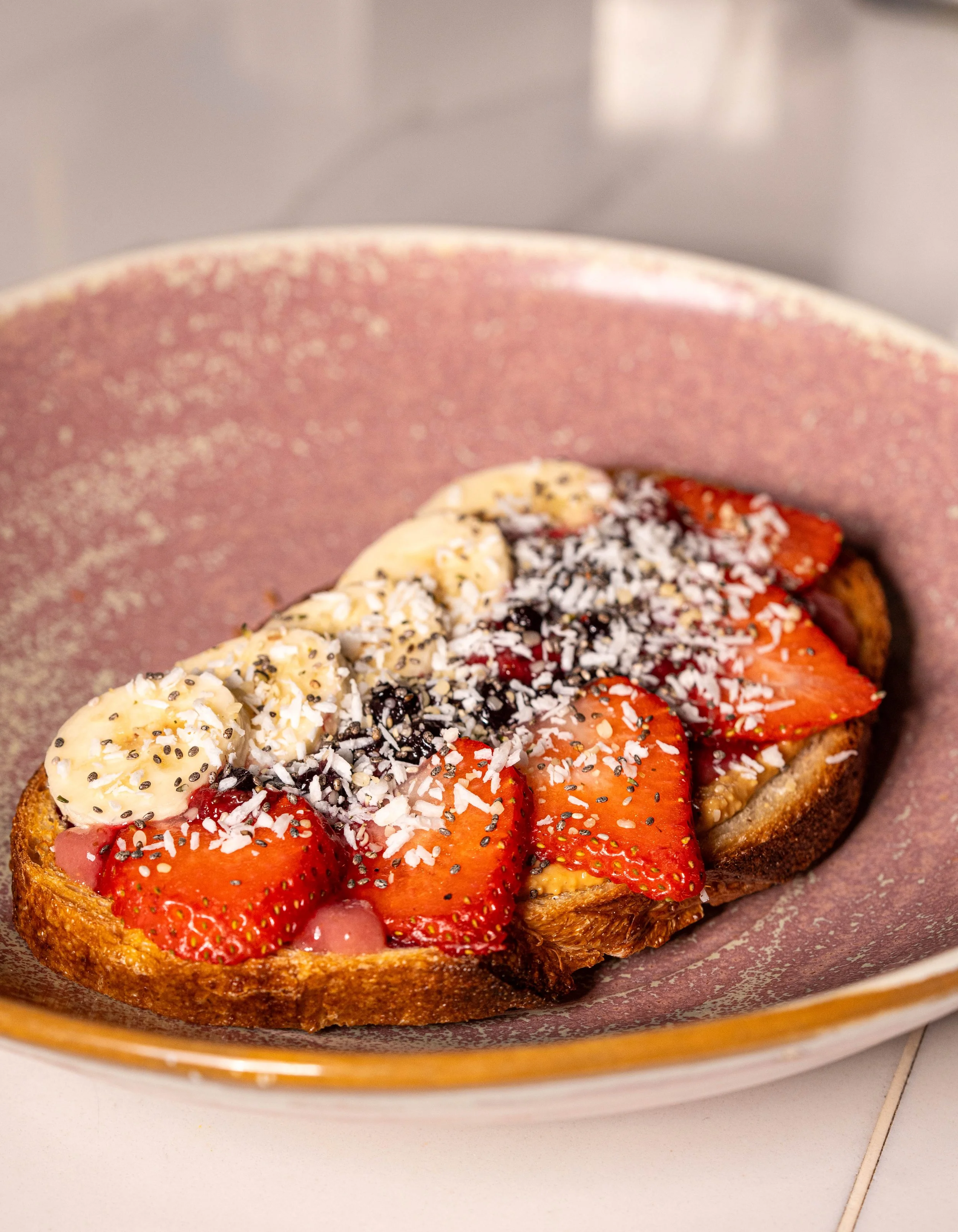 Slices of strawberries and bananas on toasted bread, topped with coconut flakes and chia seeds, served on a pink ceramic plate.