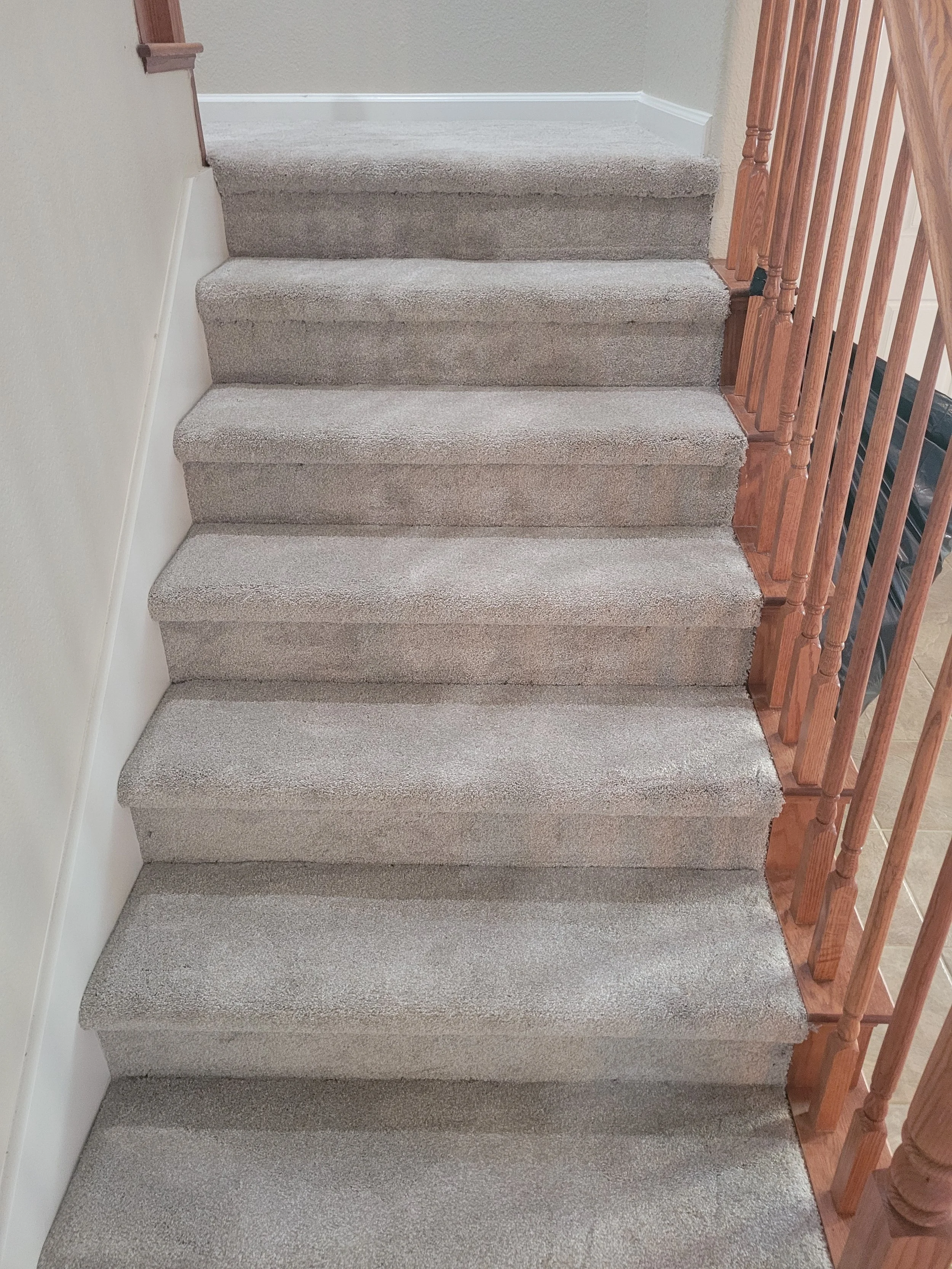 Carpeted staircase with six steps, wooden railing on the right side, beige wall on the left side, and white trim at the top of the stairs.