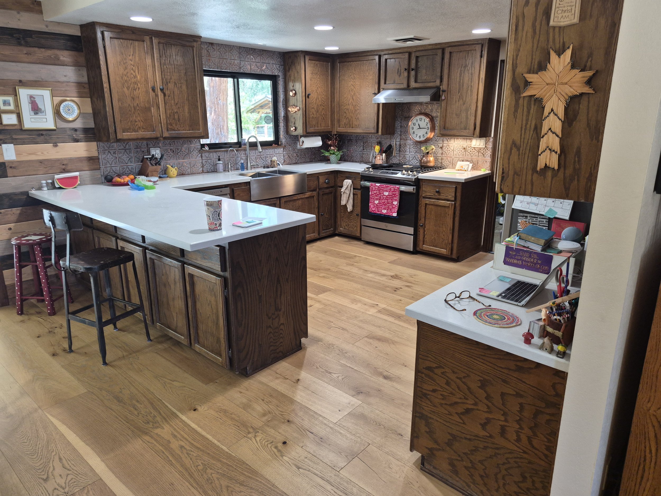 A kitchen with wooden cabinets, a large white island, and a window above the sink. The countertop has a few items including a yellow Pikachu toy, fruit, and kitchen utensils. The wall behind the stove features decorative tiles, and there is a clock a