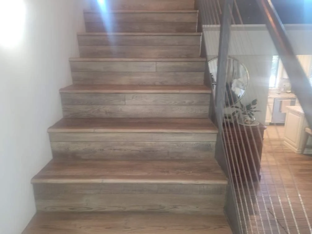 Wooden staircase with a glass railing and a plant on the landing, leading to the upper floor of a house.