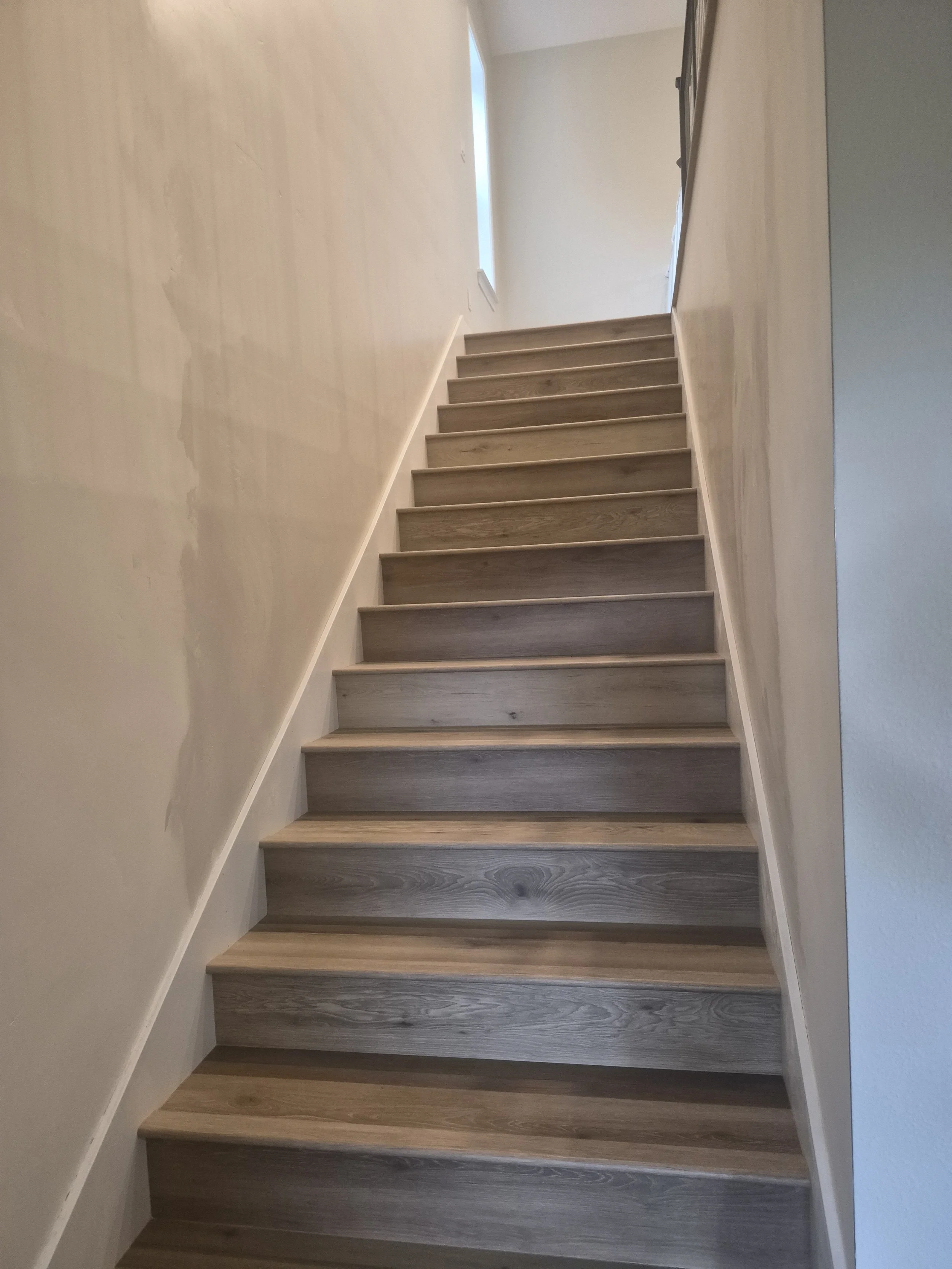 Wooden staircase with light-colored walls and a small window at the top.