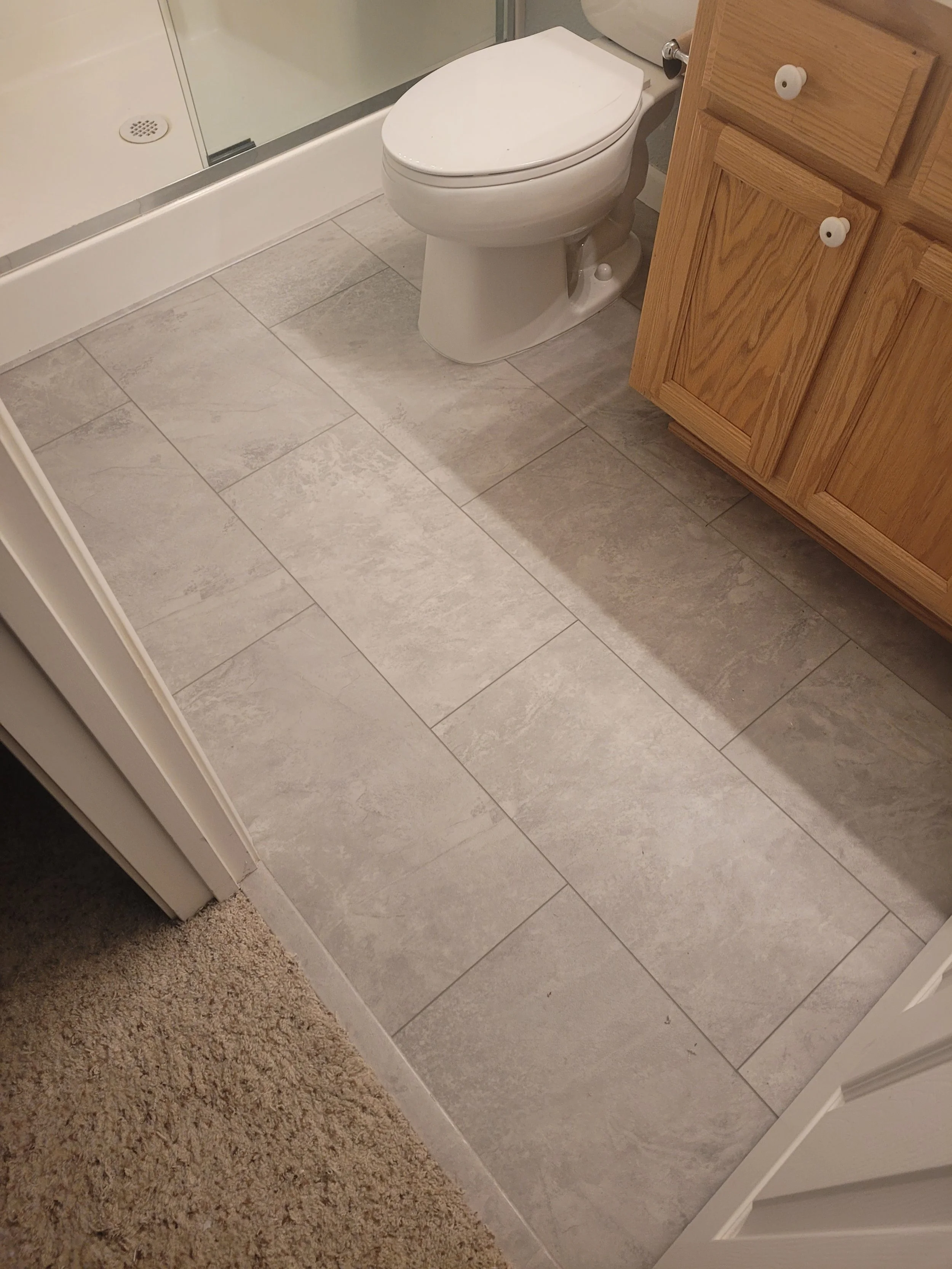 Bathroom with beige tile flooring, a white toilet, and a wooden cabinet.