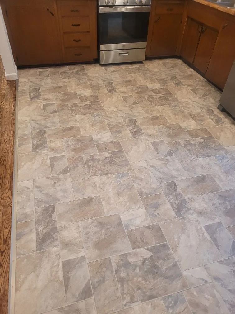Kitchen with tan and gray tile flooring, wooden cabinets, stainless steel stove, and part of a stainless steel refrigerator.
