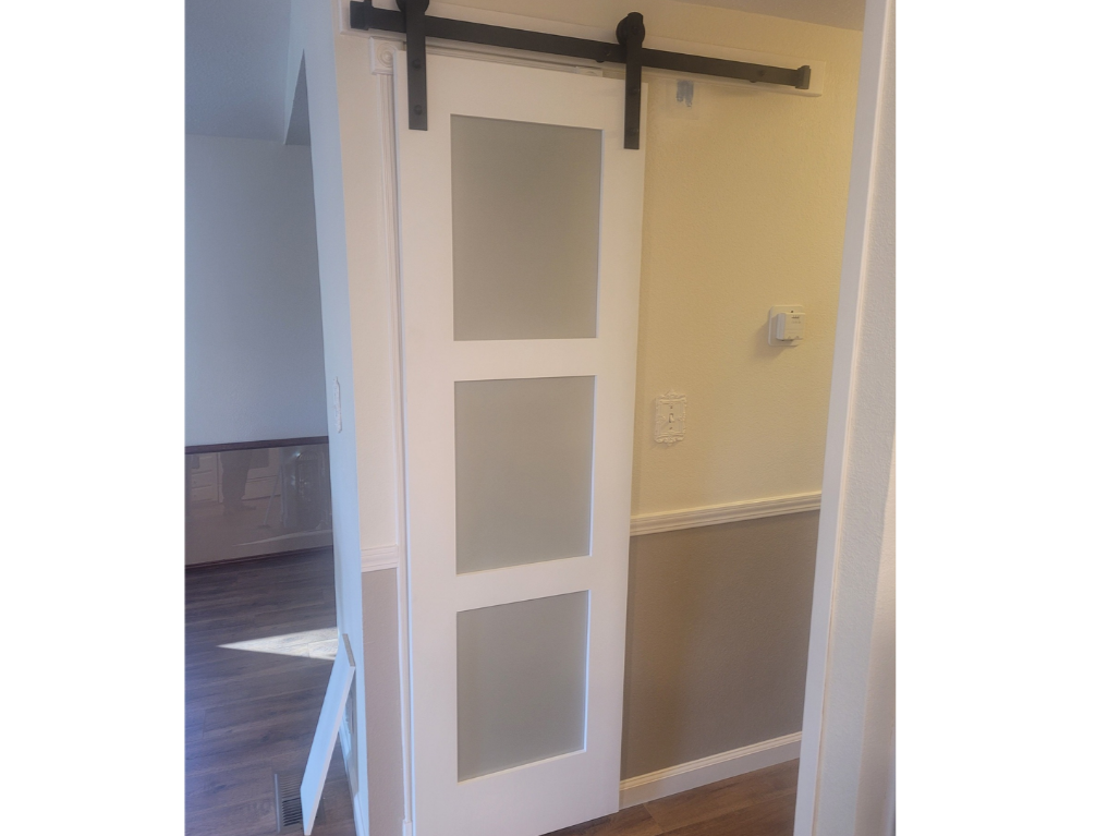 A white sliding barn door with three frosted glass panels, mounted on a black metal track, installed within a residential interior.