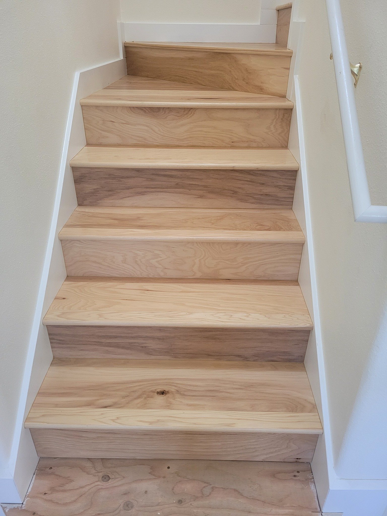 Wooden staircase with white risers and beige walls on either side.
