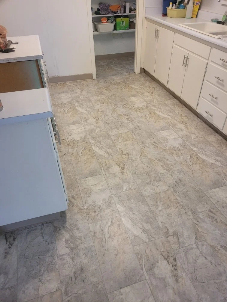 Kitchen with white cabinets, beige tiled floor, and some cleaning supplies on the countertop.