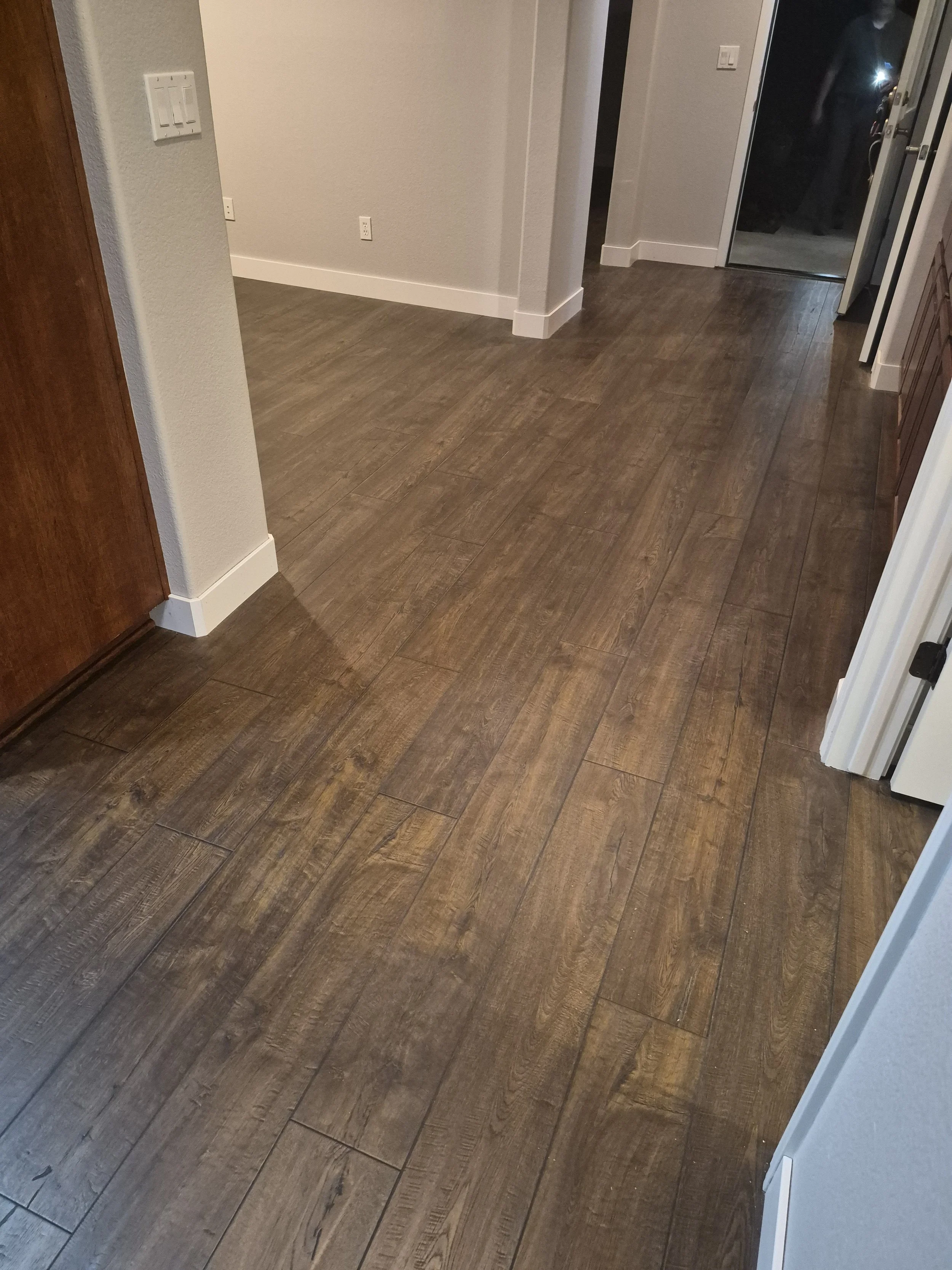 Wood flooring in an interior hallway with white and wood cabinets and a sliding glass door leading outside.