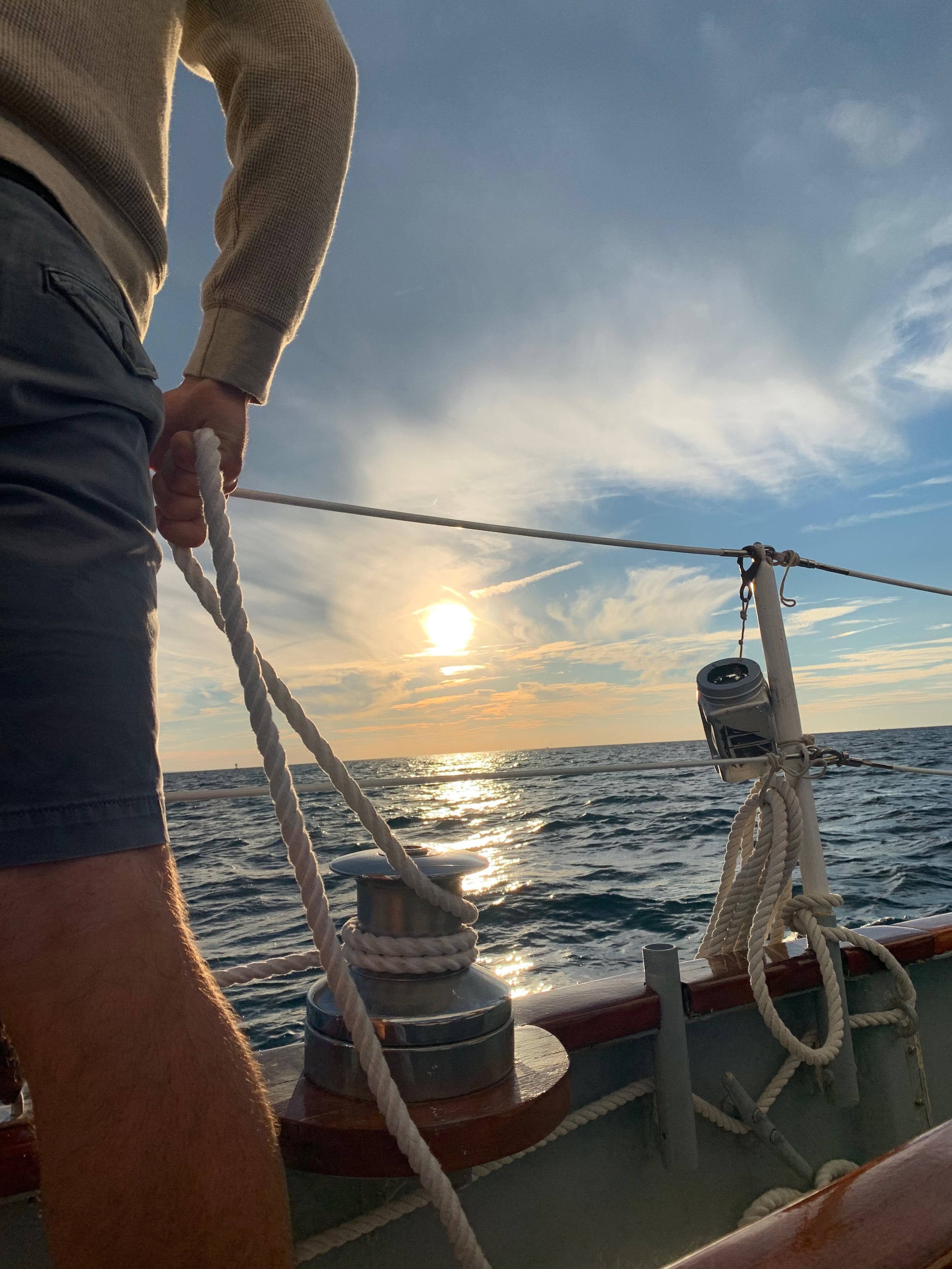 Person holding rope on sailboat with ocean sunset view