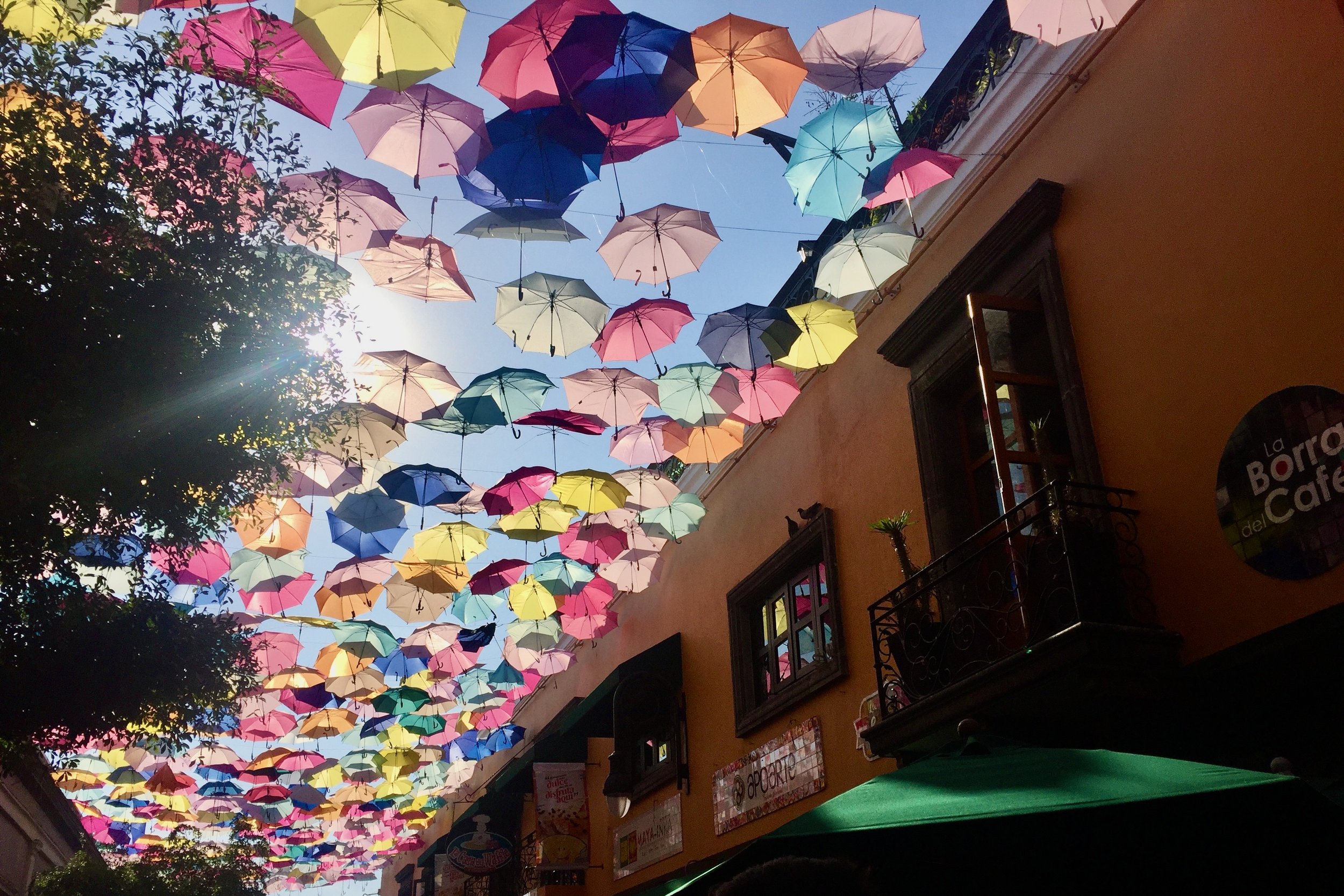 Colorful umbrellas hanging in the sky between buildings, creating a vibrant canopy in a sunny street.