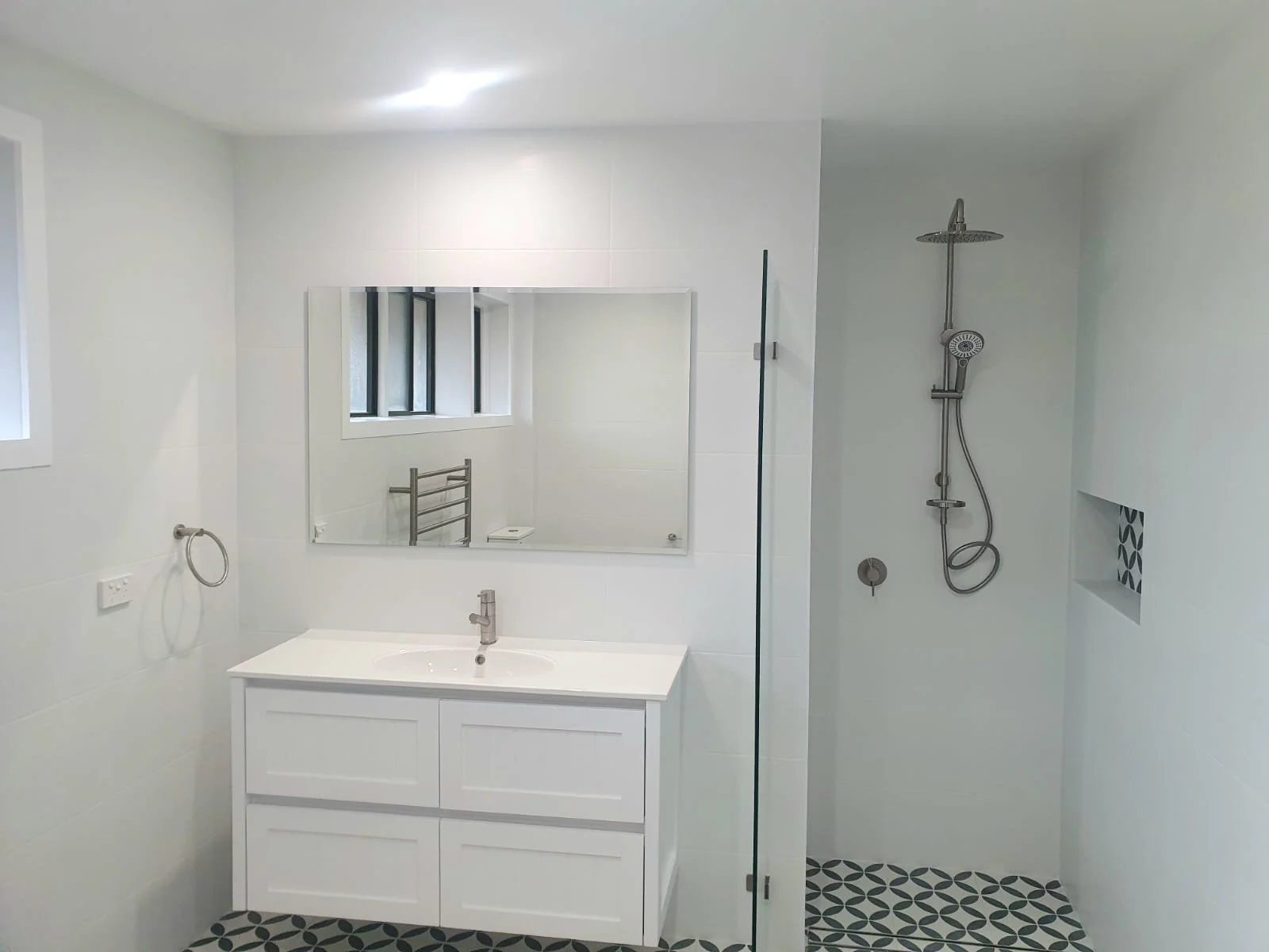 Modern bathroom with beige tiles, featuring a glass shower enclosure, toilet, metal grab bar, and towel rack.
