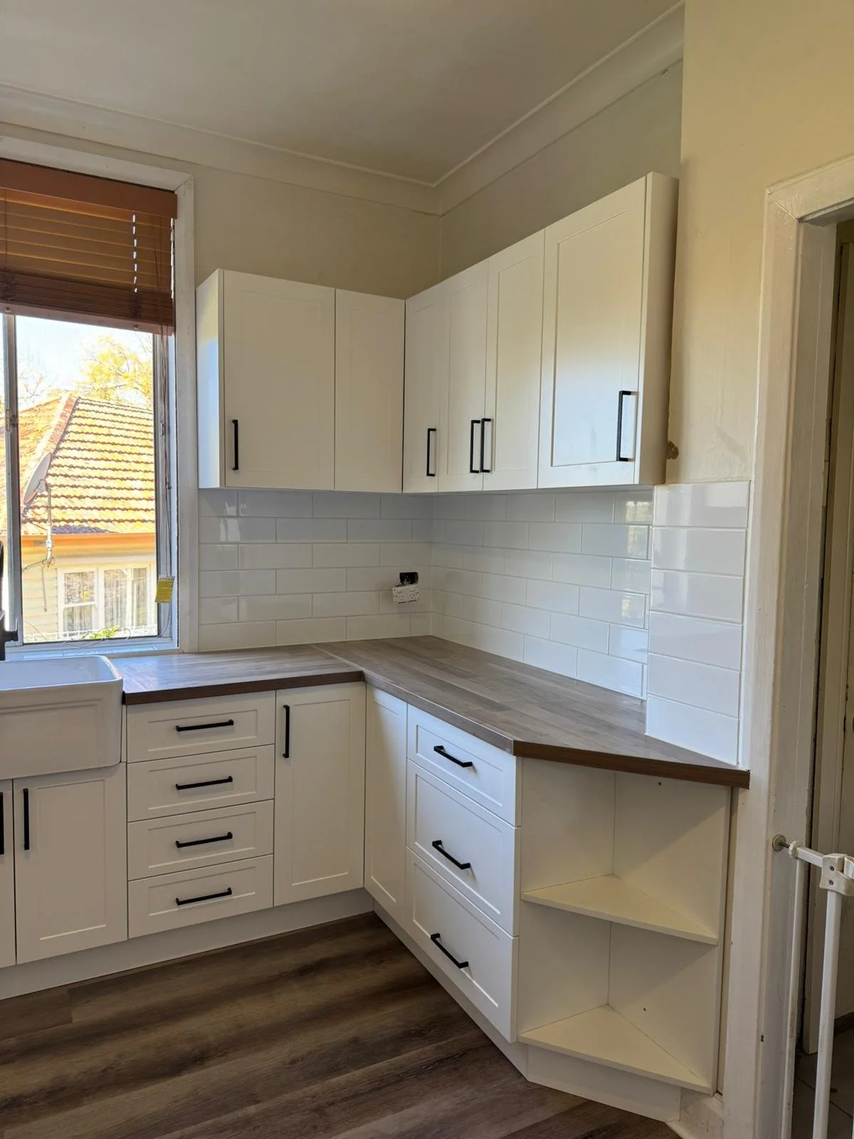 Kitchen with white cabinets, wooden countertop, white subway tile backsplash, window with blinds, and wood flooring.