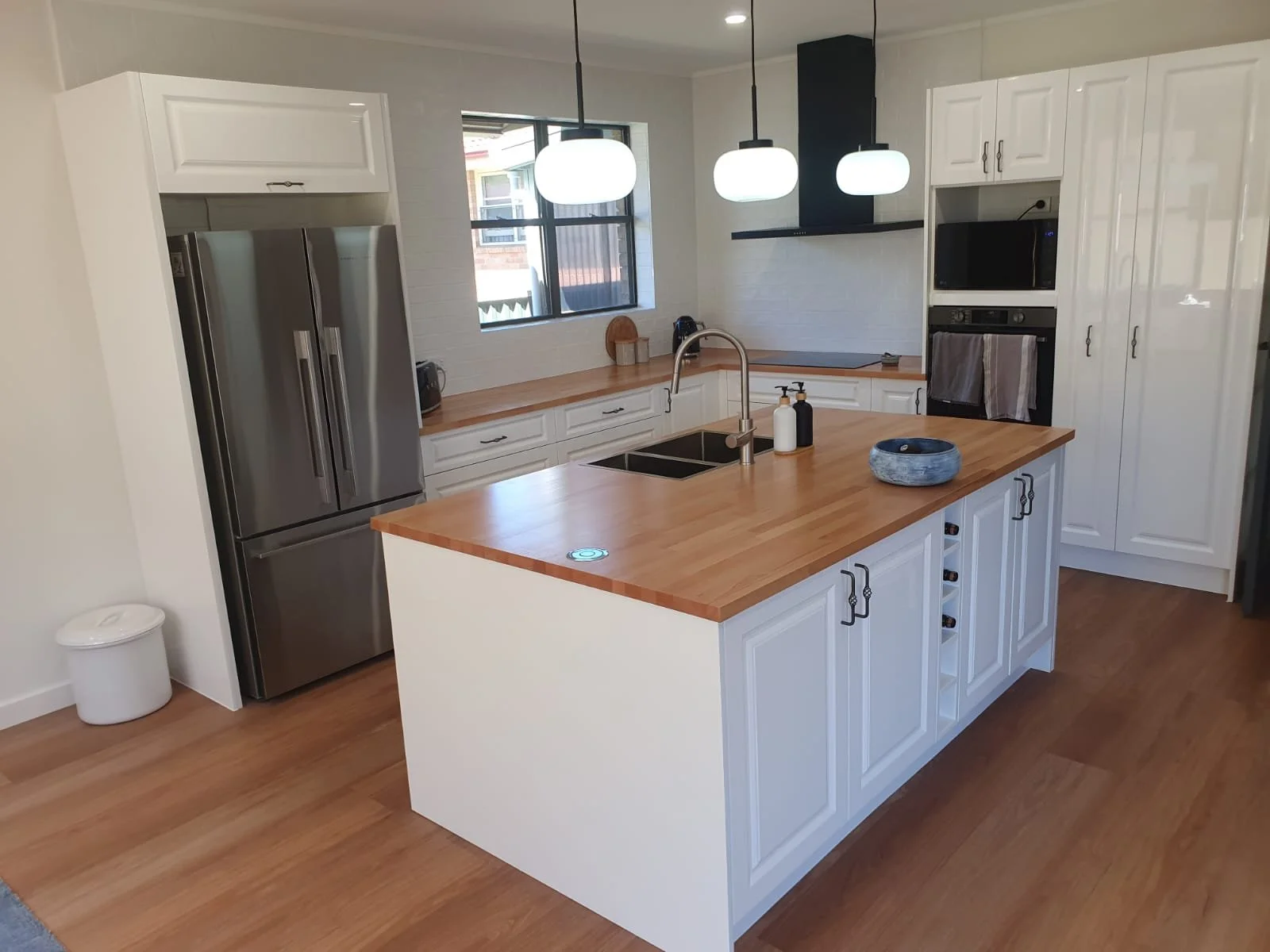 Small kitchen with white cabinets, brown countertops, a stainless steel sink, gas stove, and wooden flooring.