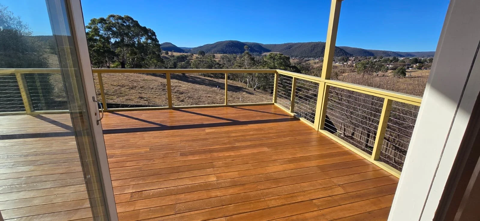 Wooden deck with glass doors and lush green plants nearby.