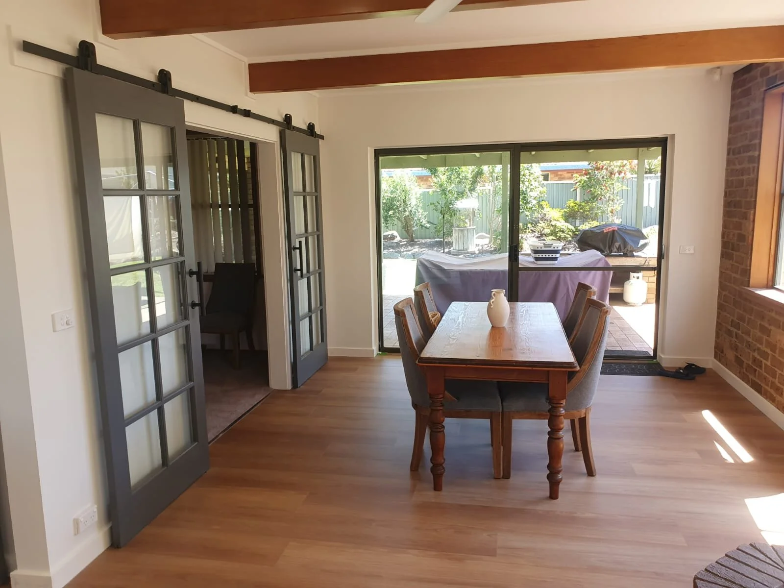 Dining room with a wooden table and six chairs, large sliding glass doors leading to a backyard garden, and a brick accent wall.