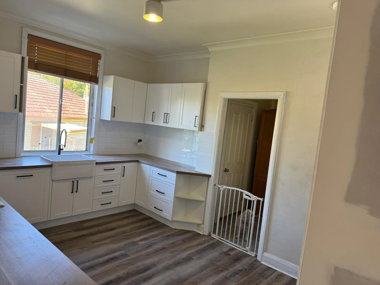 Kitchen with white cabinets, a window above the sink, and a small pet gate in front of a door, with wood-look flooring.