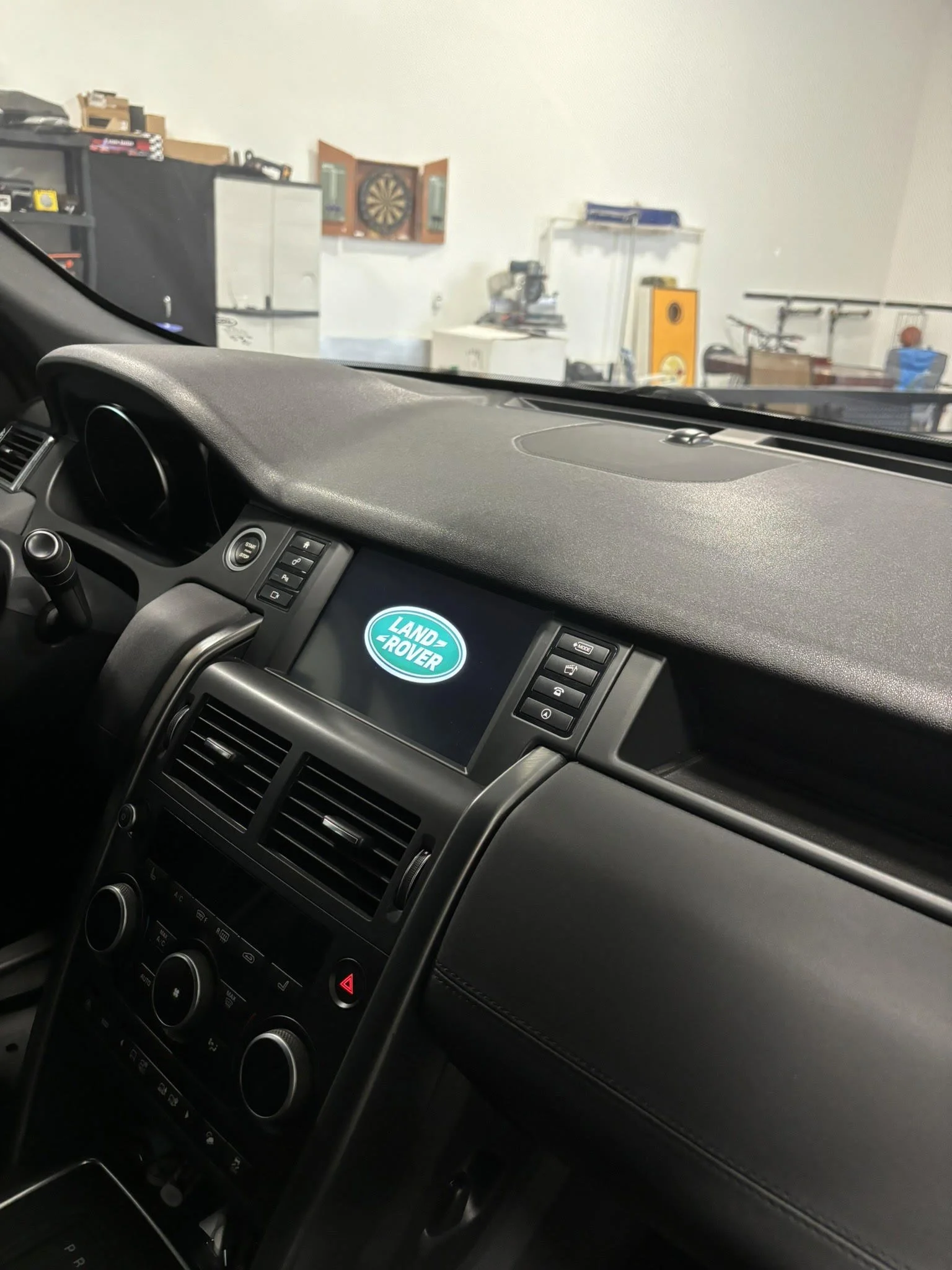 The interior of a Land Rover vehicle showing the dashboard with the Land Rover logo on the screen, air vents, and control buttons.