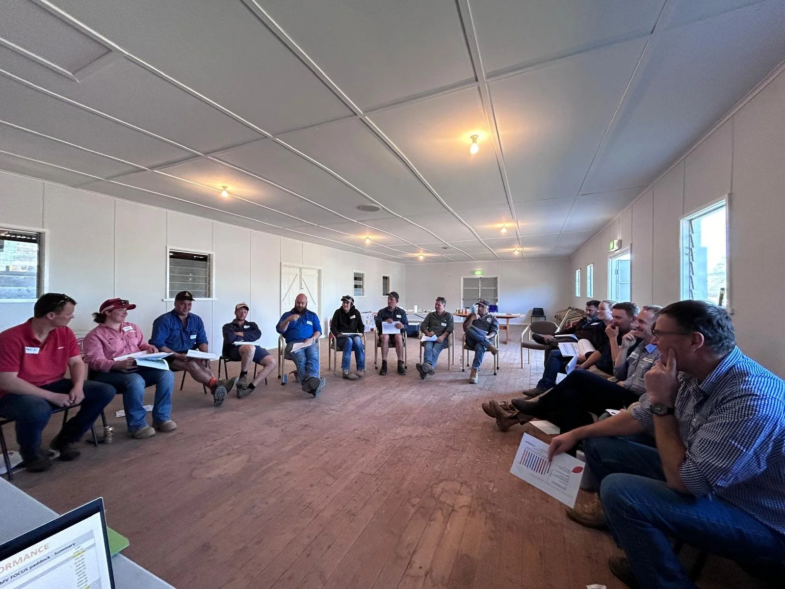 Group of individuals sitting in a semi-circle in a spacious room, participating in a meeting or discussion.