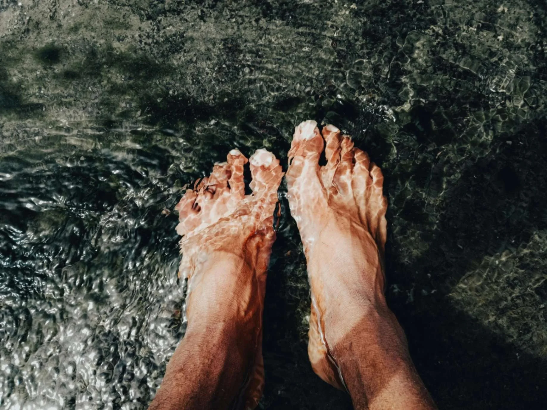 Person standing in clear water, visible feet and lower legs, shallow water surface with ripples