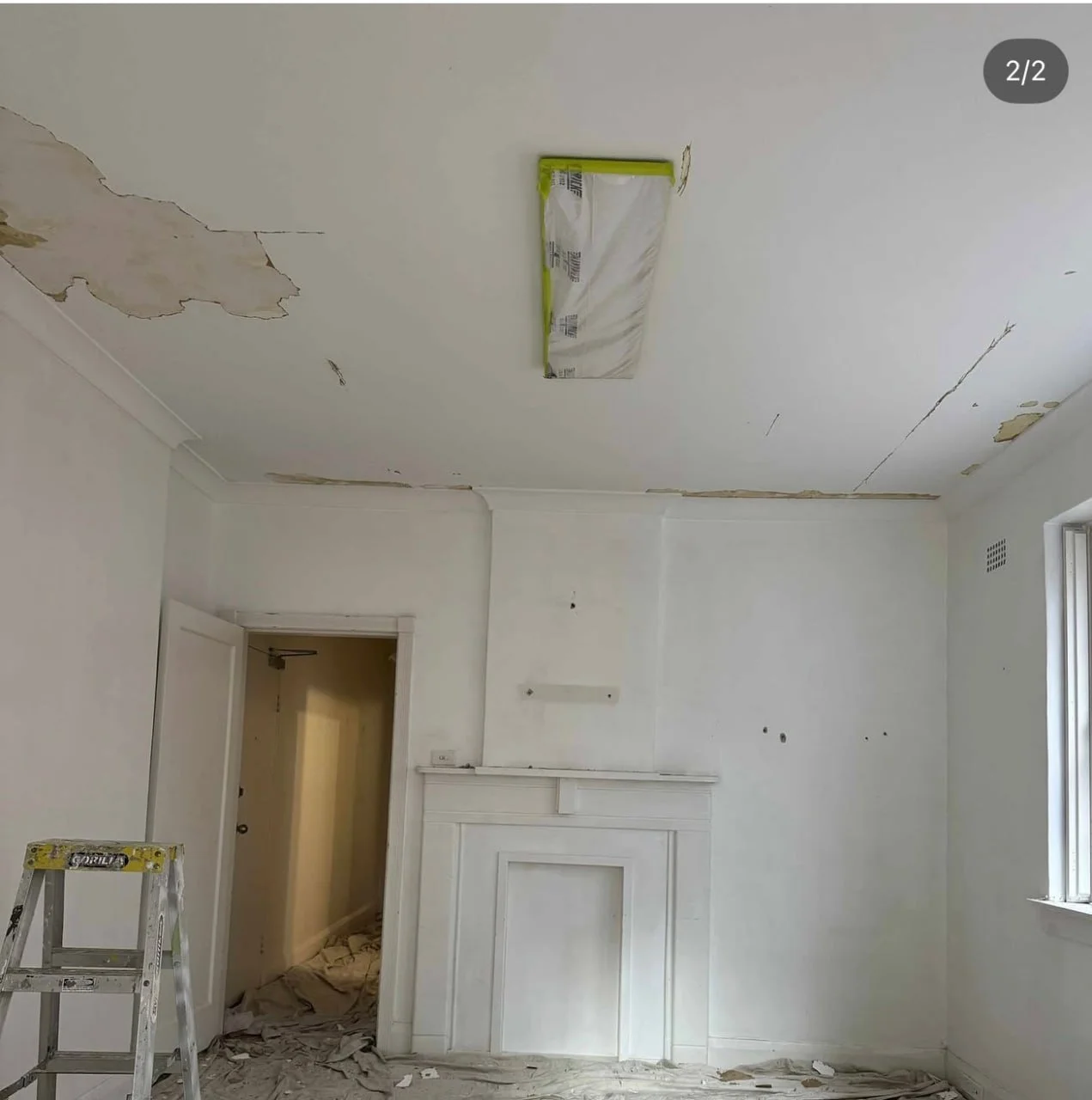 Room undergoing renovation with peeling paint on ceiling, a ladder, and debris on the floor.