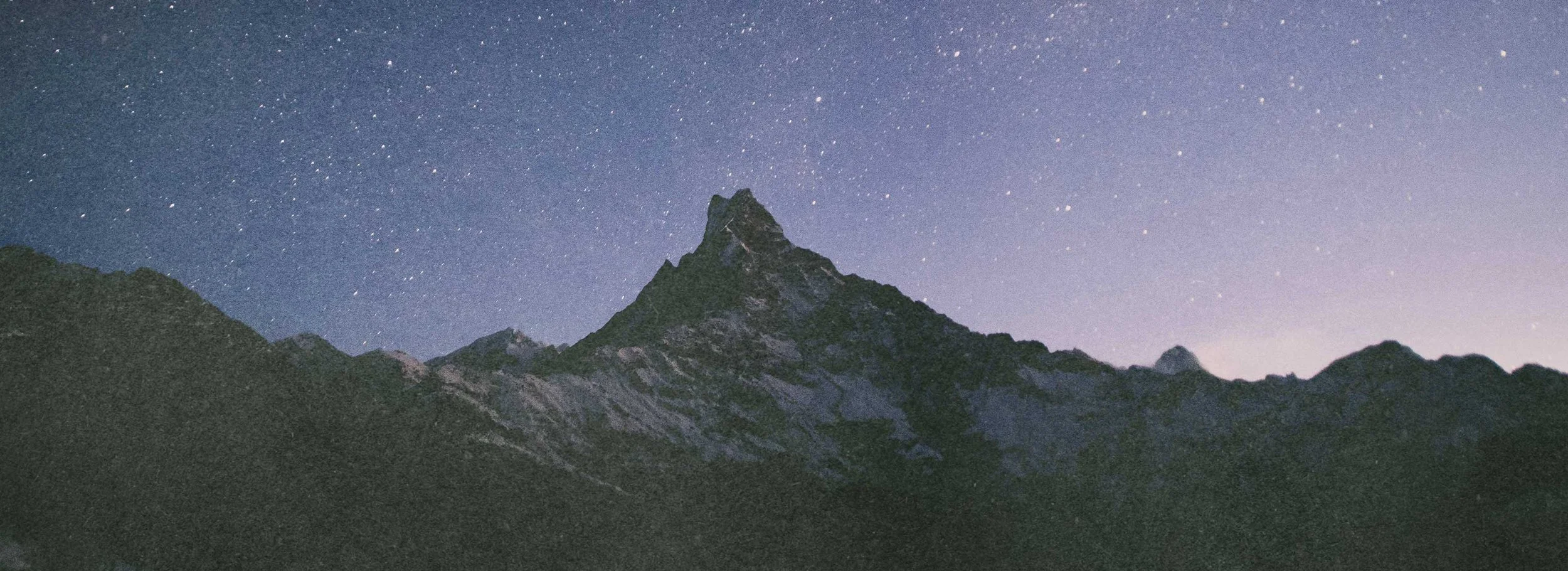 Nighttime view of a mountain with a sharp peak, set against a star-filled sky