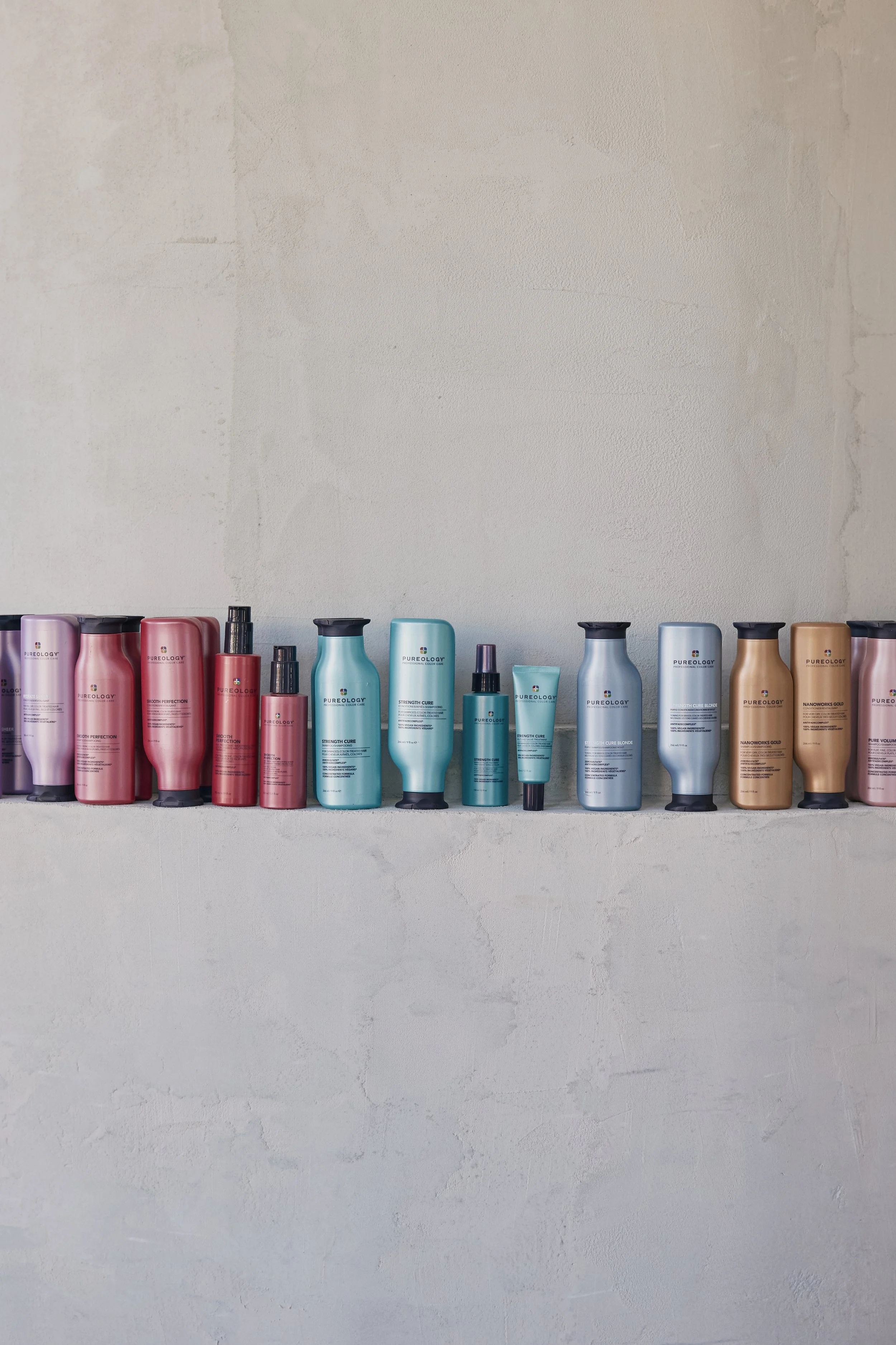 Line of colorful shampoo and conditioner bottles on a white wall shelf.