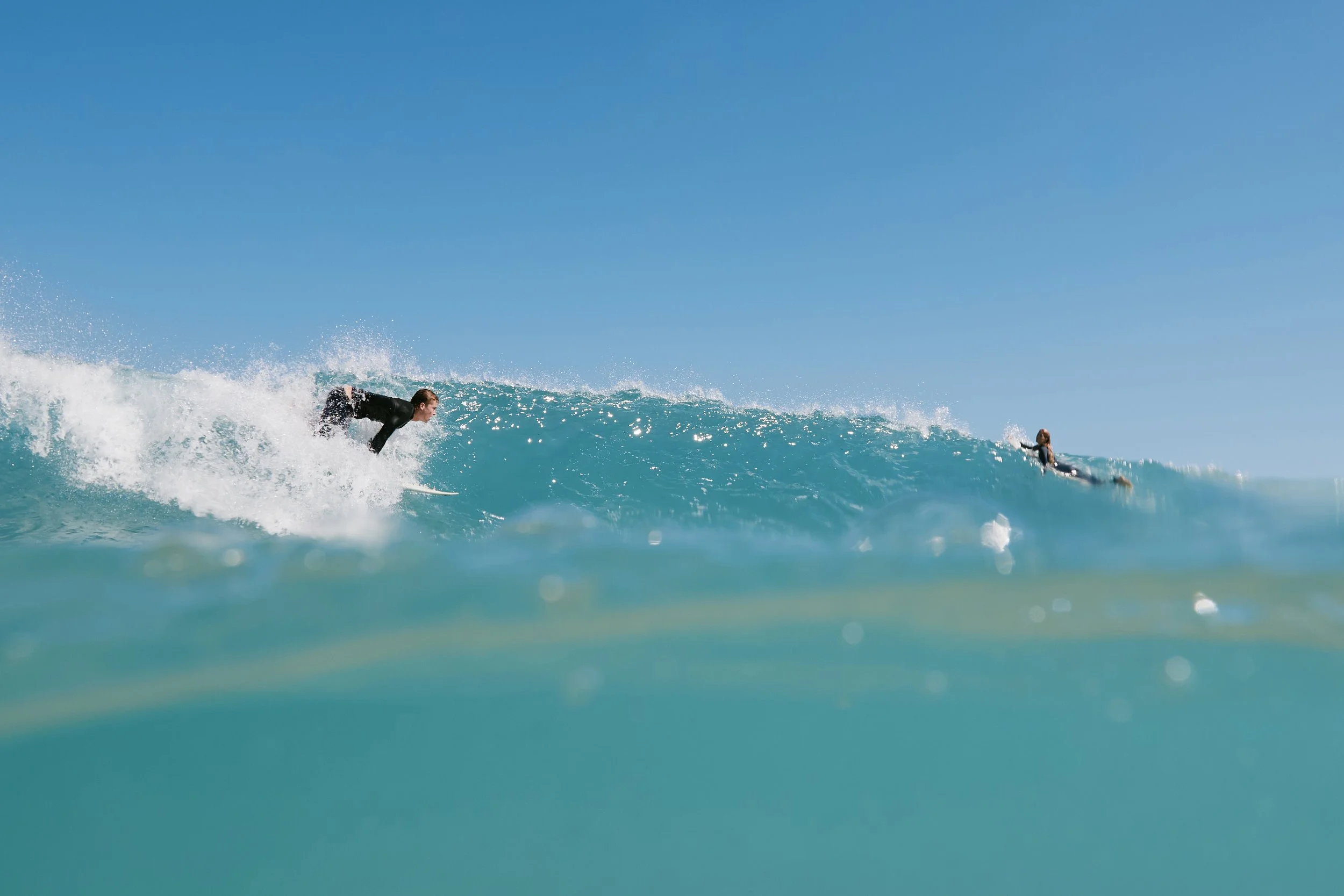 A person surfing on a blue wave in clear ocean water under a bright blue sky.