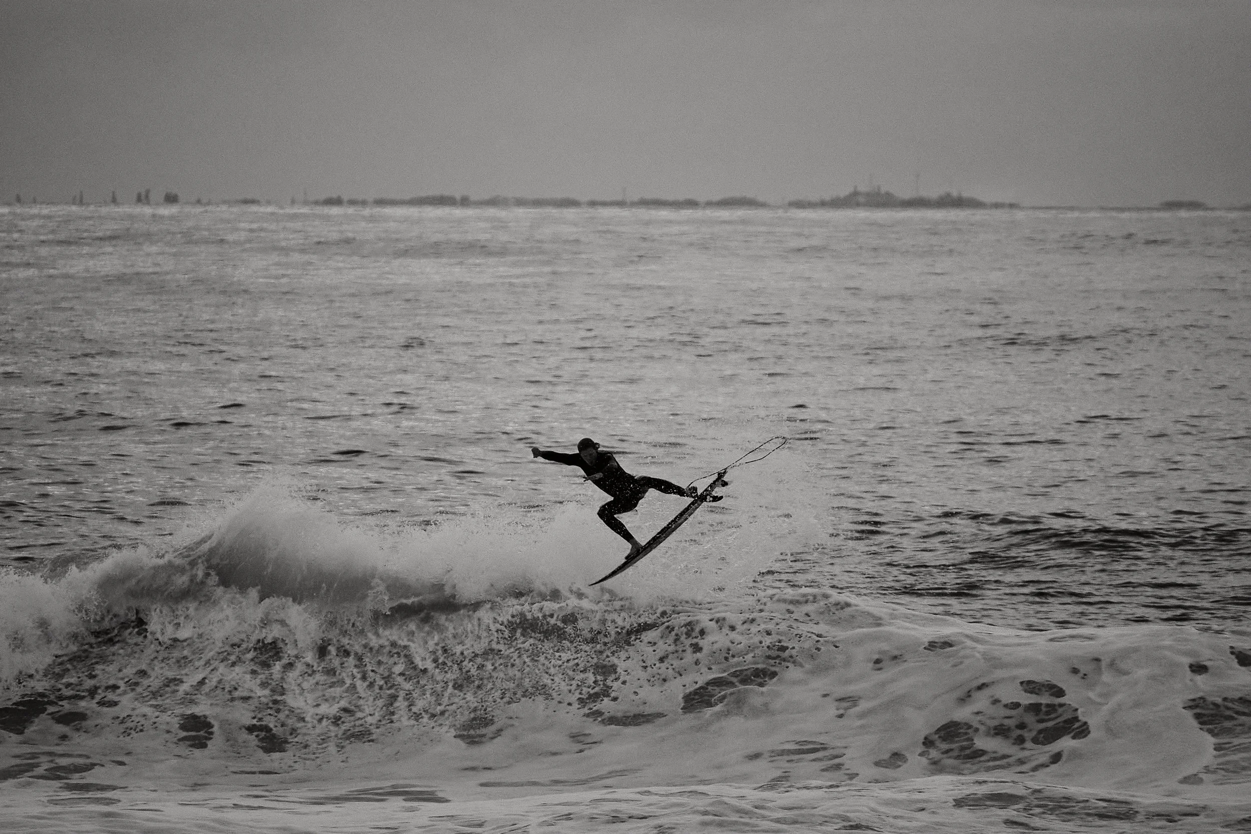 A person surfing on a wave in the ocean, captured in black and white.