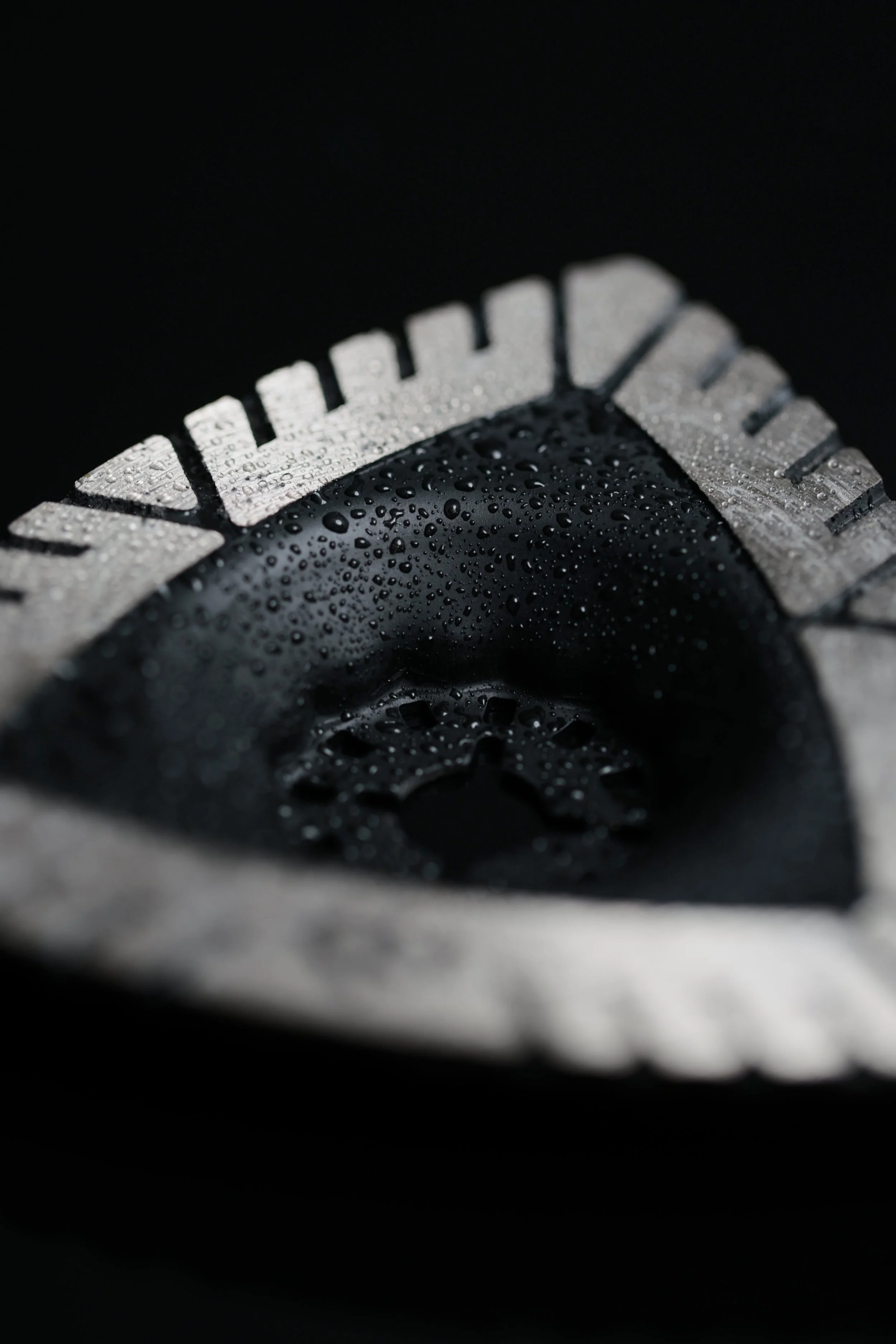 Close-up of a black and silver automotive tire tread with water droplets on its surface.