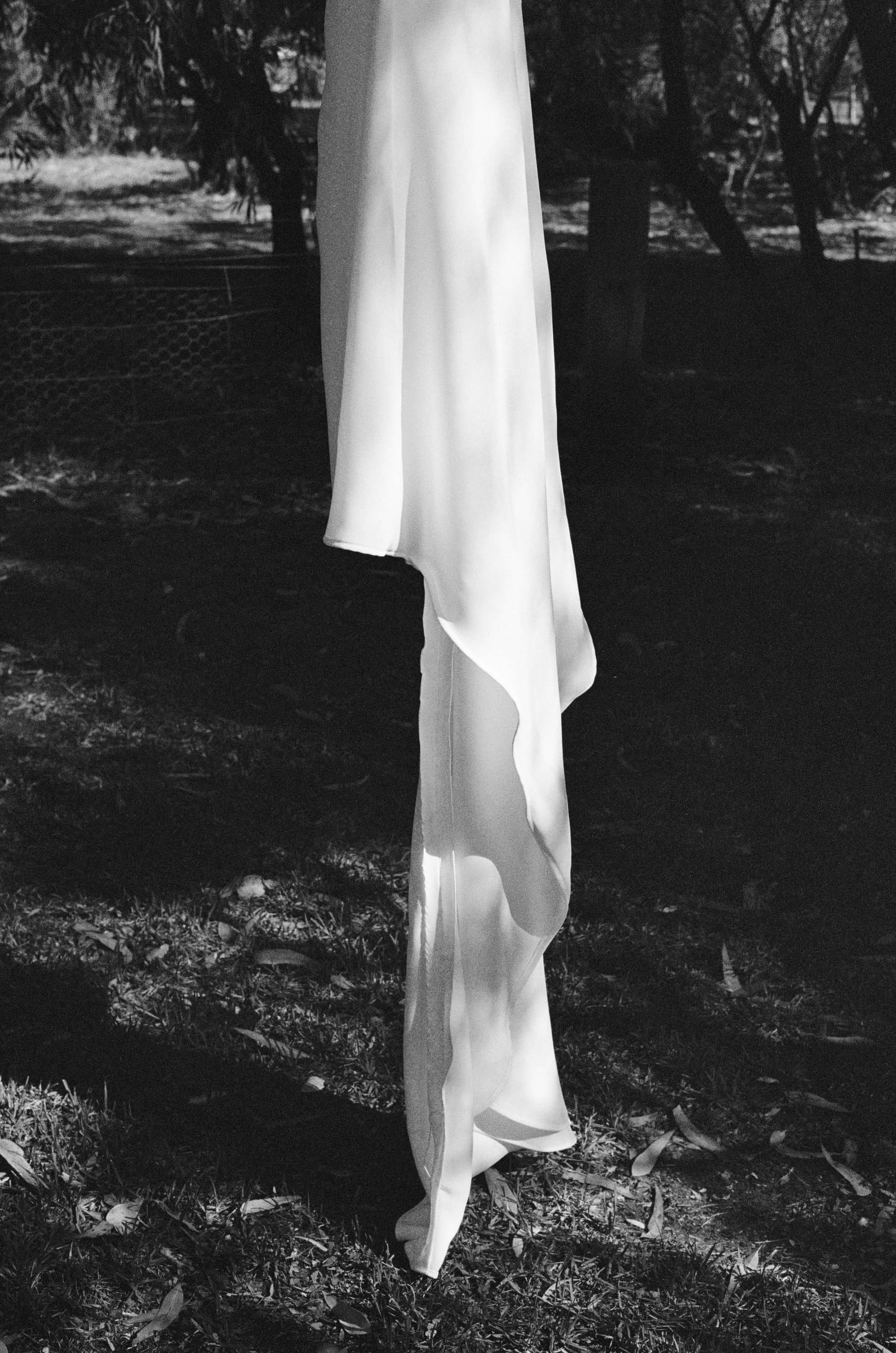 A black and white photo of a piece of fabric hanging from a pole outdoors, with trees and a fence visible in the background.
