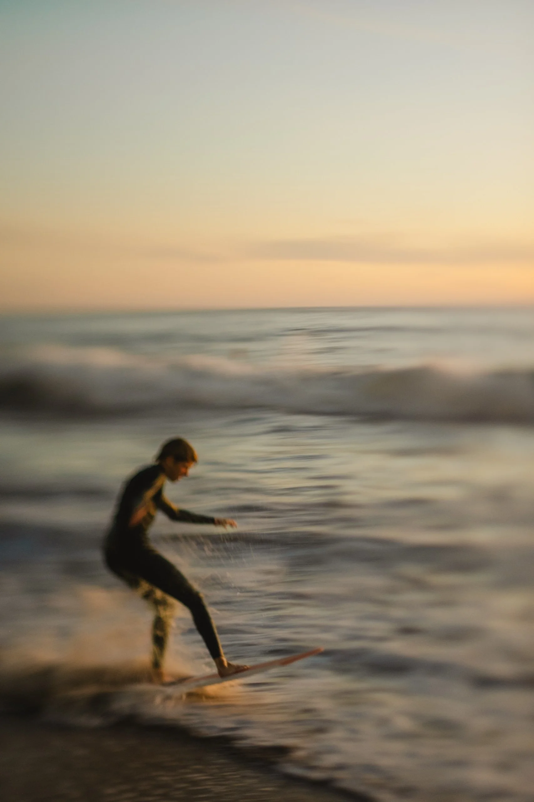 A person in a wetsuit riding a surfboard on the ocean during sunset or sunrise.