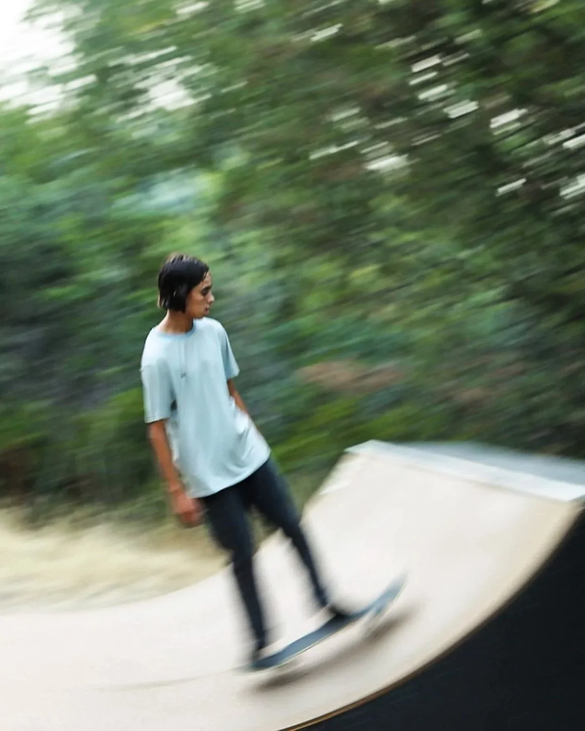 A person skateboarding on a ramp at a skate park with blurred green trees in the background.