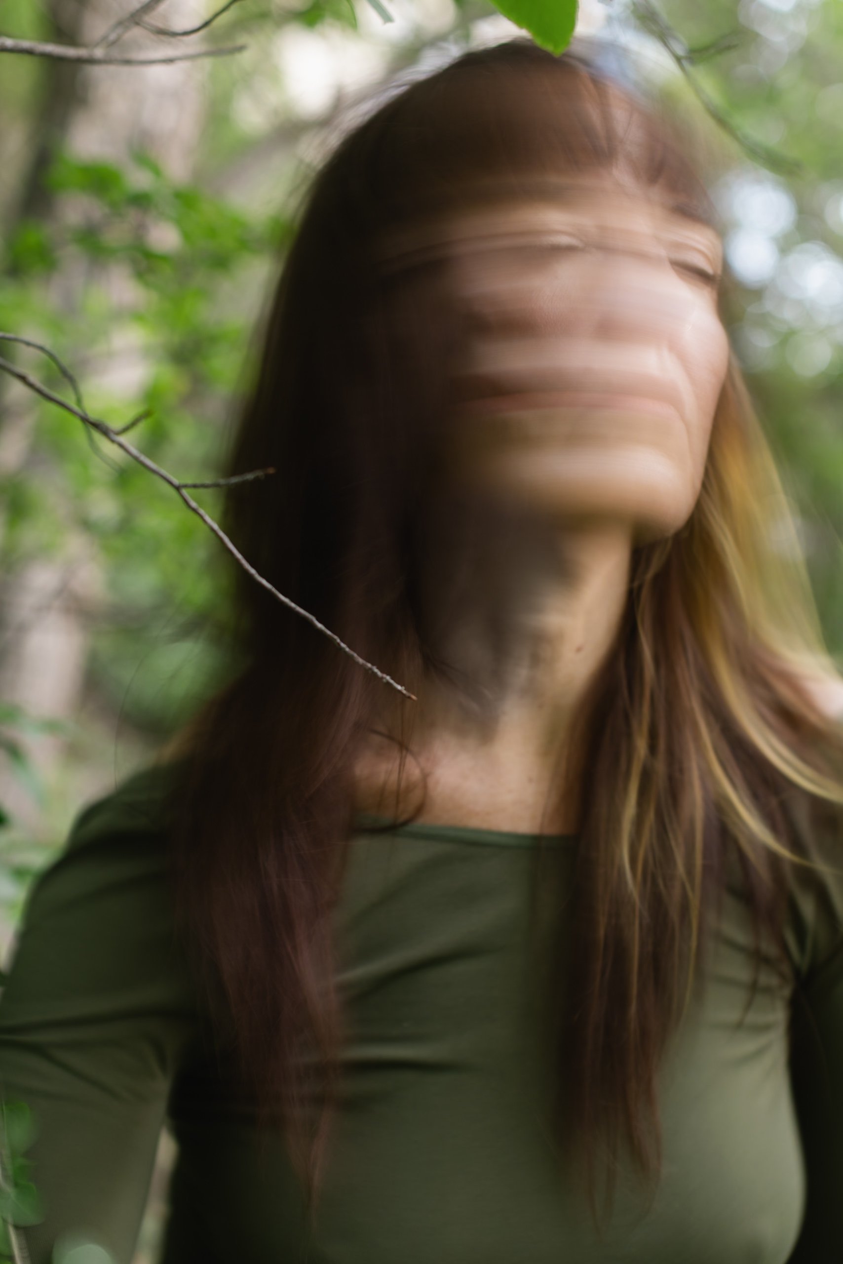 Blurred image of a woman with long hair outdoors among green foliage, with a motion effect that causes her face and part of her hair to appear smeared.