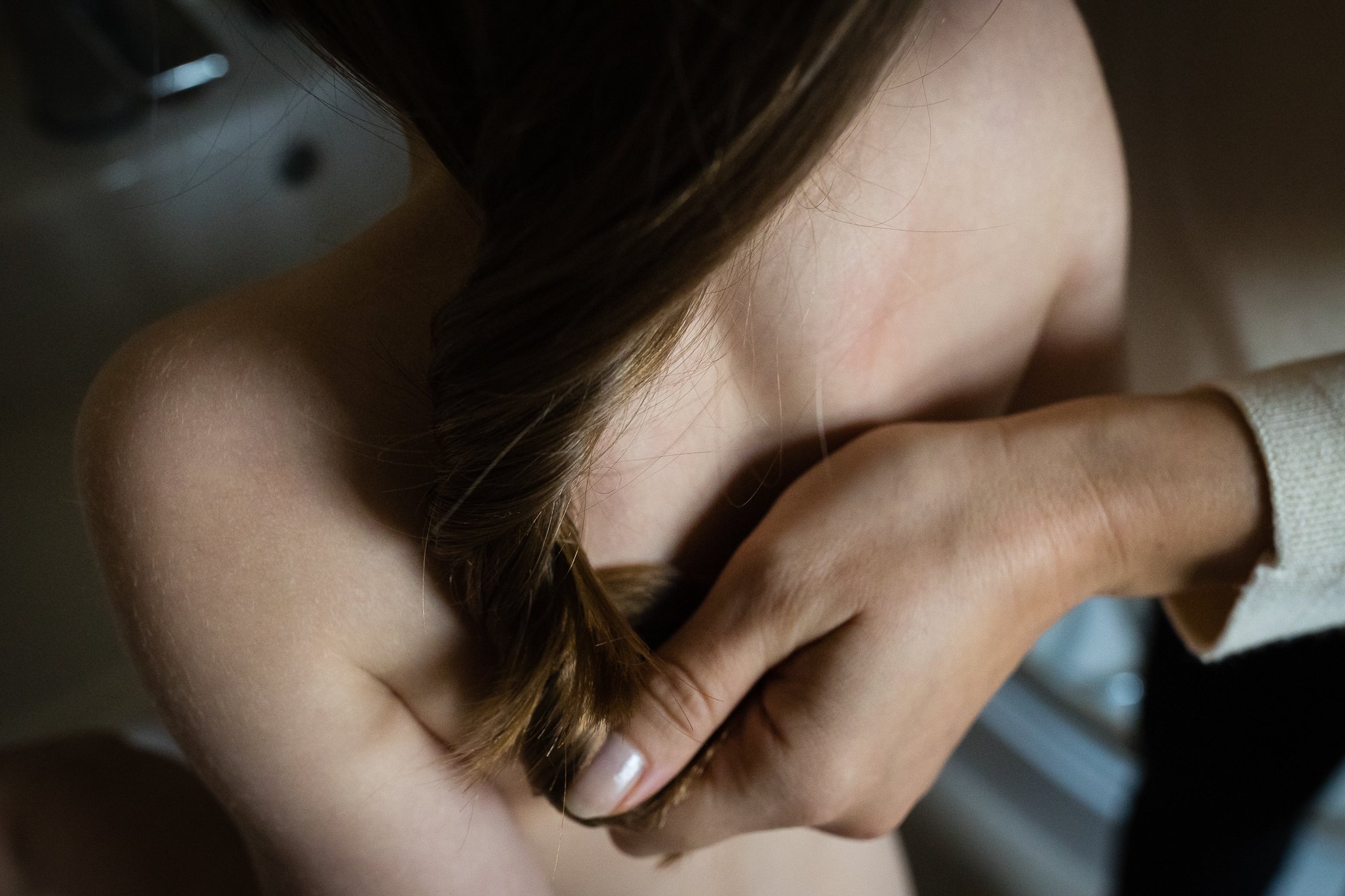 Close-up of a woman's shoulder, hair, and hand gently resting on her arm, with a blurred background.