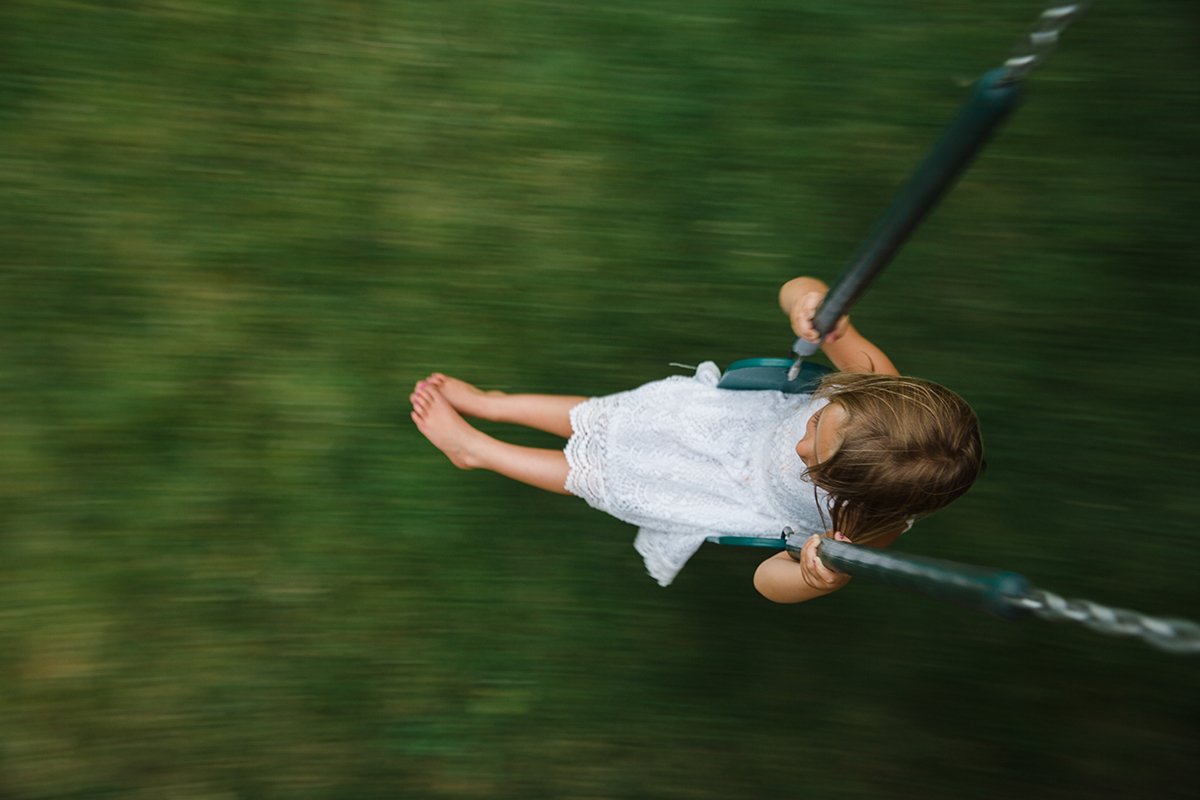 A young girl in a white dress swinging on a swing set with a blurred green background.