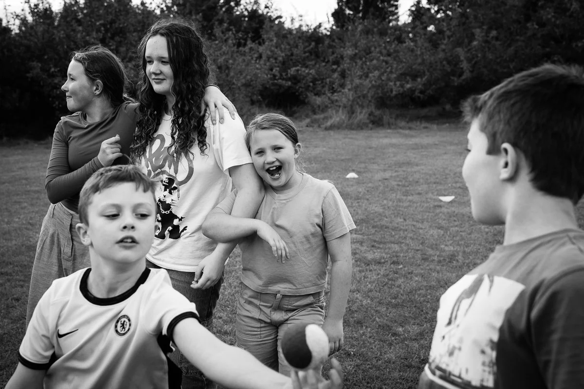 Group of children playing outdoors on the grass, some smiling and engaging in what appears to be an active game.