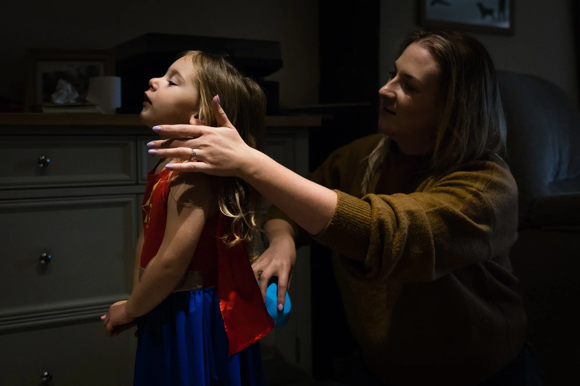 A woman is taking a picture of a young girl with her eyes closed, in a dimly lit room.