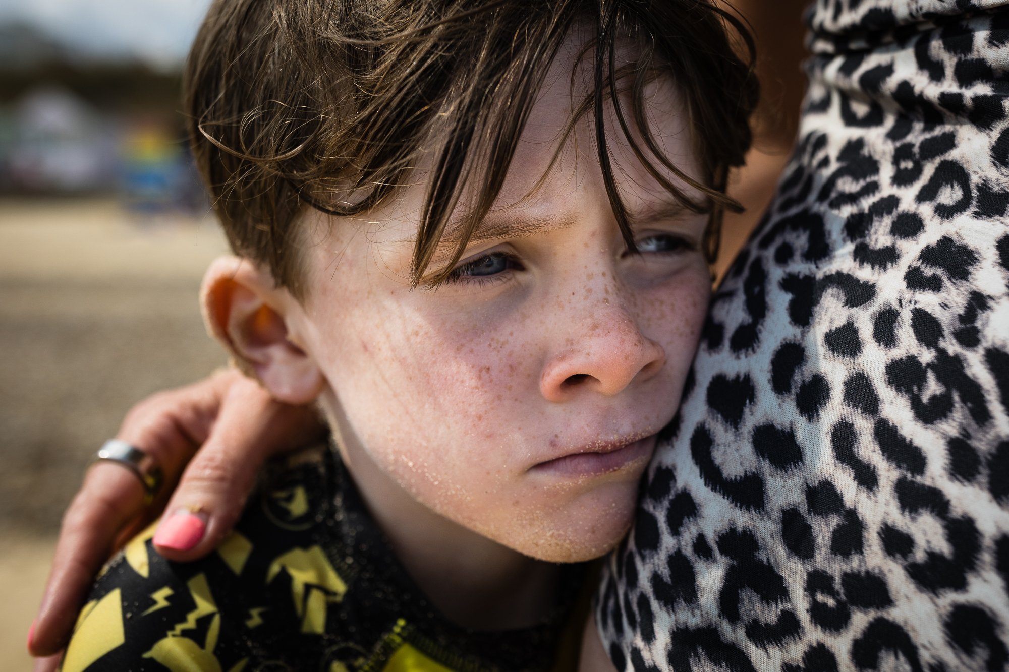 A young boy with wet brown hair and freckles being hugged by an adult wearing a leopard print shirt.