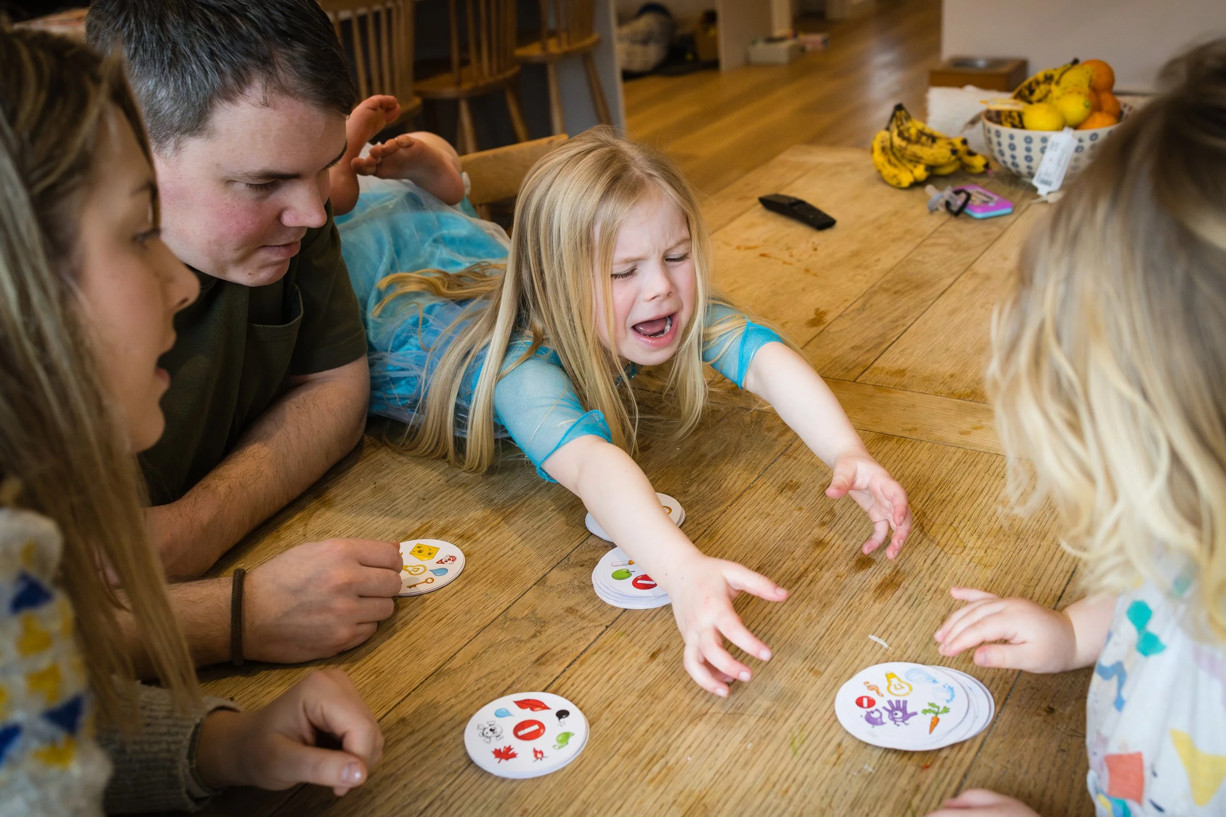 Group of children and adults playing a colorful card game at a wooden table in a cozy home.