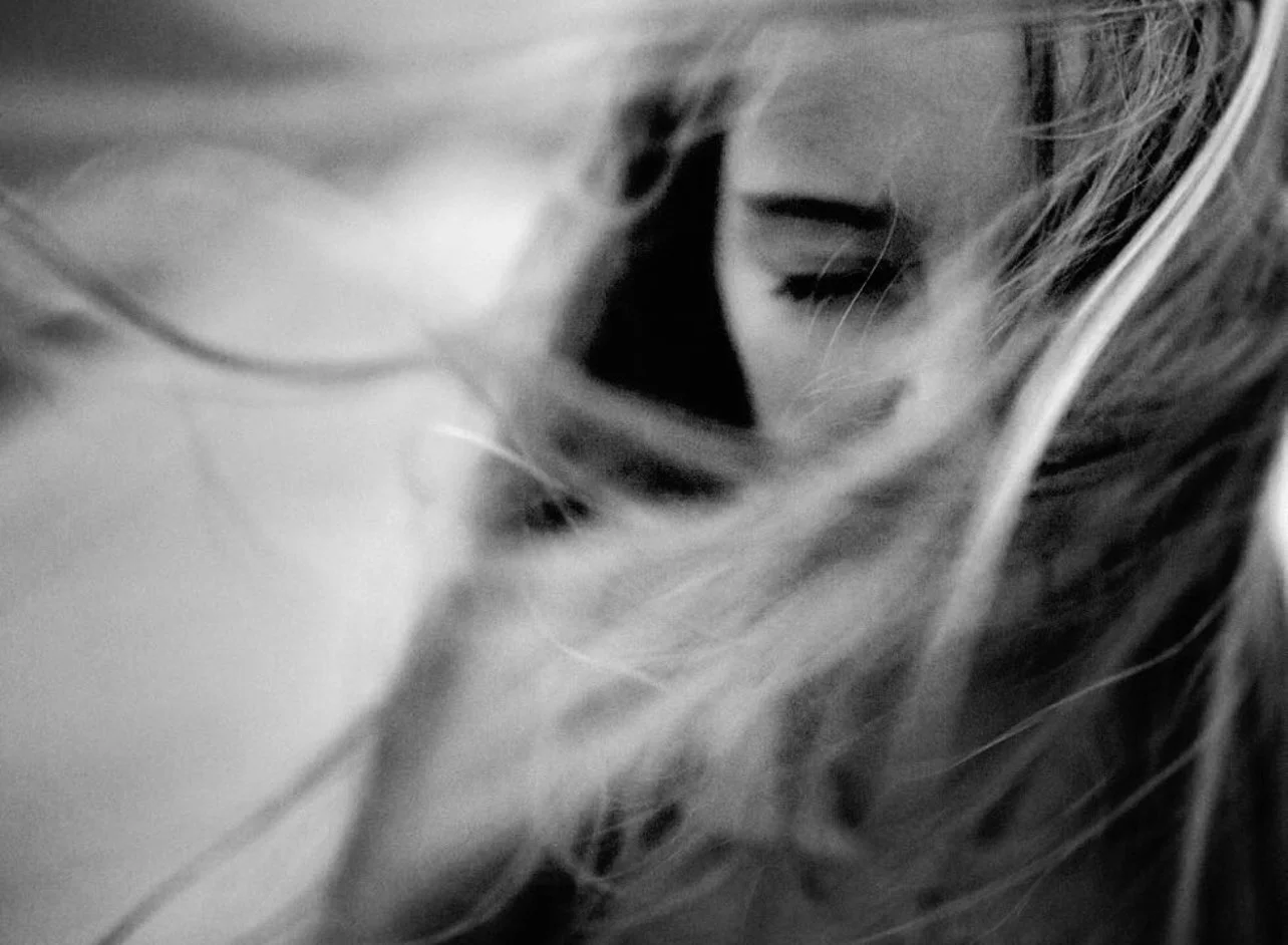 Black and white close-up photo of a woman with closed eyes, partially obscured by her hair.
