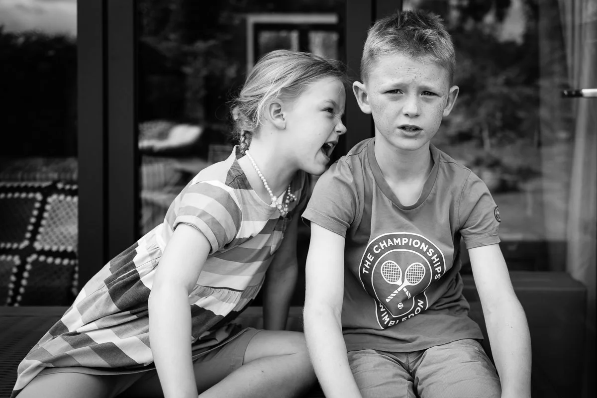 A girl appears to be shouting at a boy, who looks upset or surprised, on a patio outside a house.