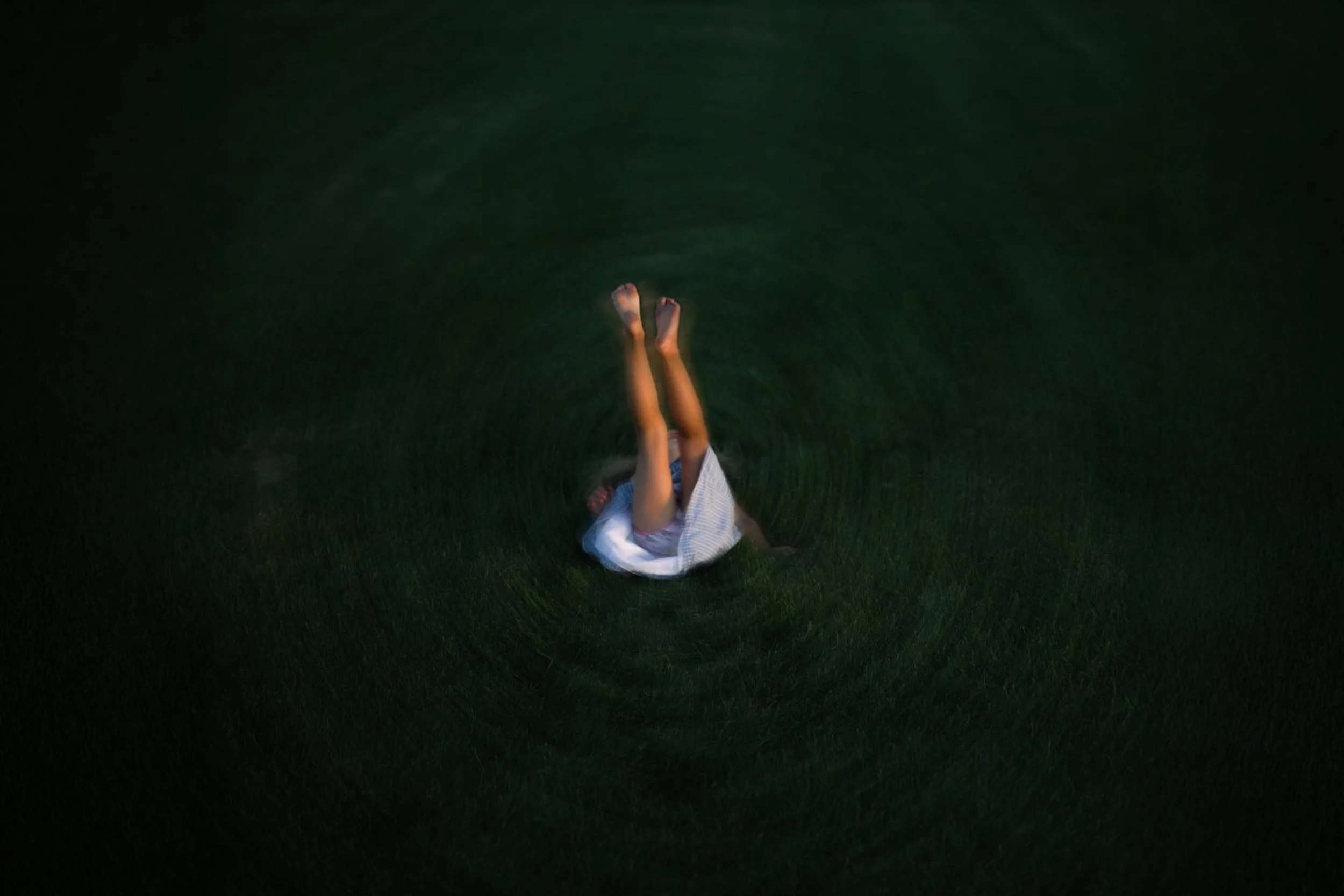 Person lying on grass field with legs raised in the air, seen from above.