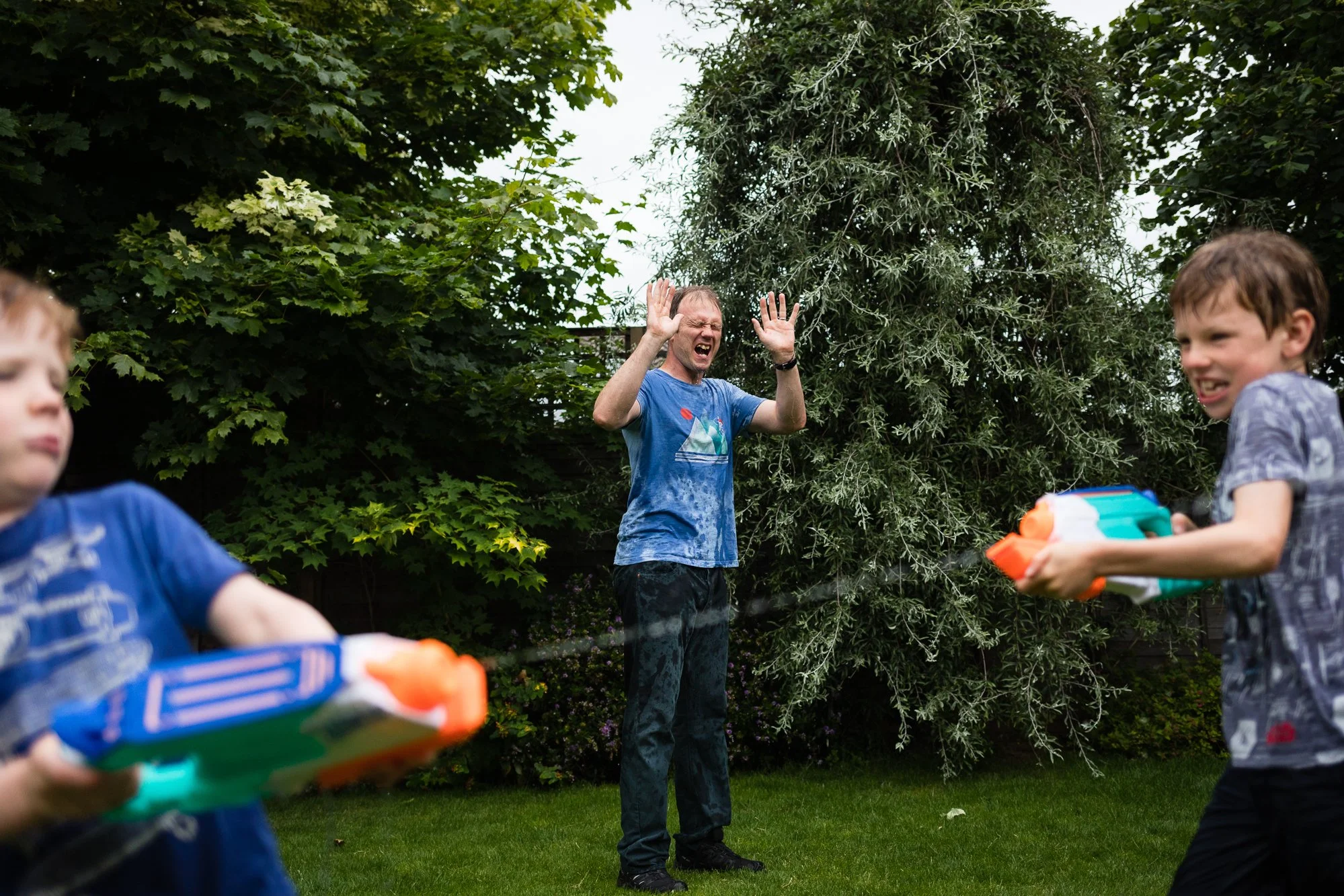 A man getting sprayed with water while playing a water gun fight with two children in a backyard during daytime.
