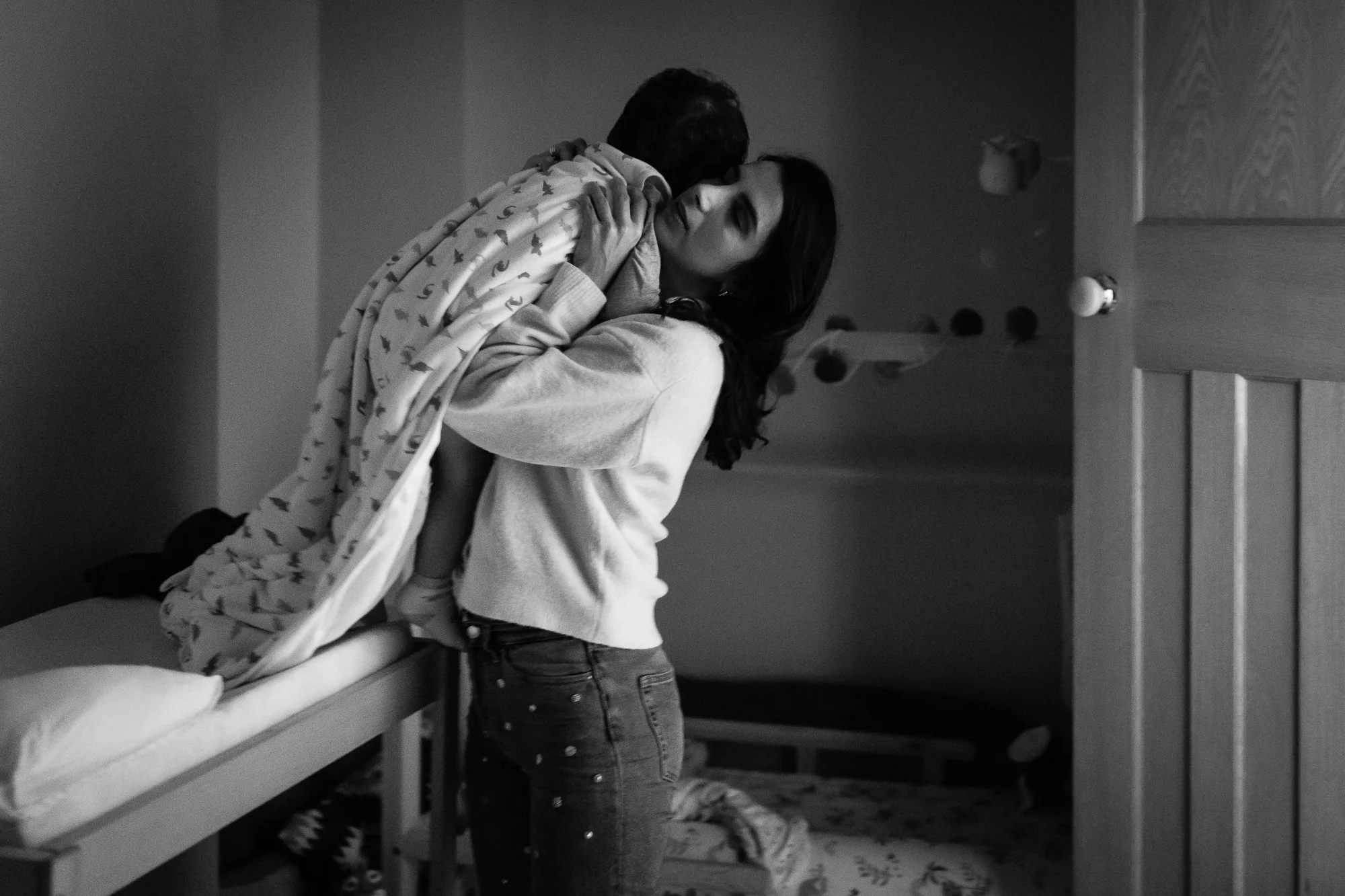 A woman and a young child sharing a joyful moment, with the woman lifting the child in the air, in a dimly lit room.