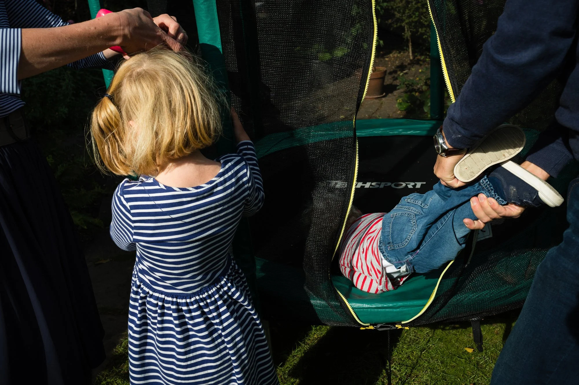 A young child in striped clothing is being helped into a portable changing station by two adults.