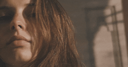 Close-up of a woman's face with brown hair, partially visible, in a dimly lit room.